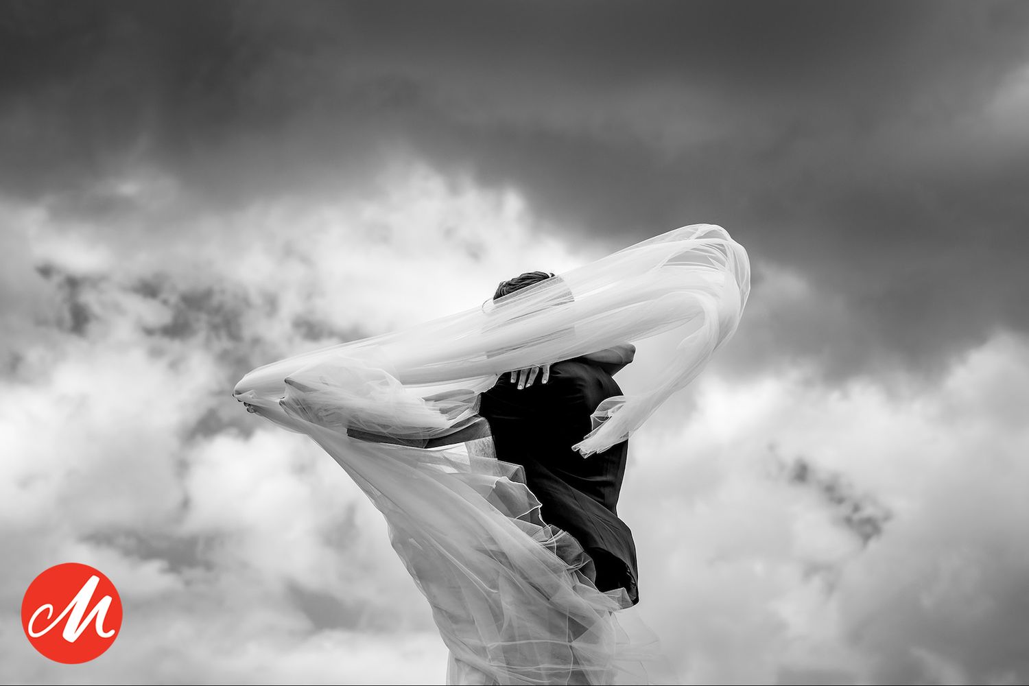 A flowing white veil billows dramatically against a dark stormy sky in black and white artistic photography.