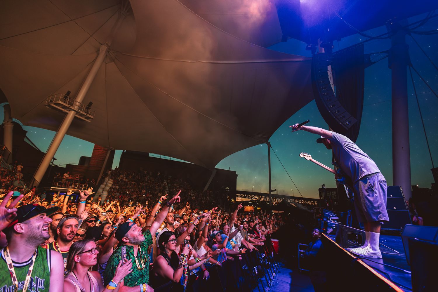 Dynamic concert scene with performer jumping on stage while crowd cheers under dramatic purple lighting.