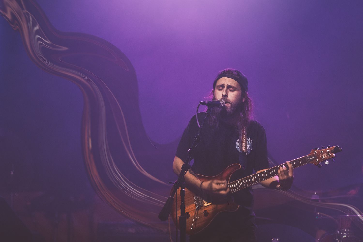 Musician performing with guitar against purple backdrop with ethereal smoke effects.