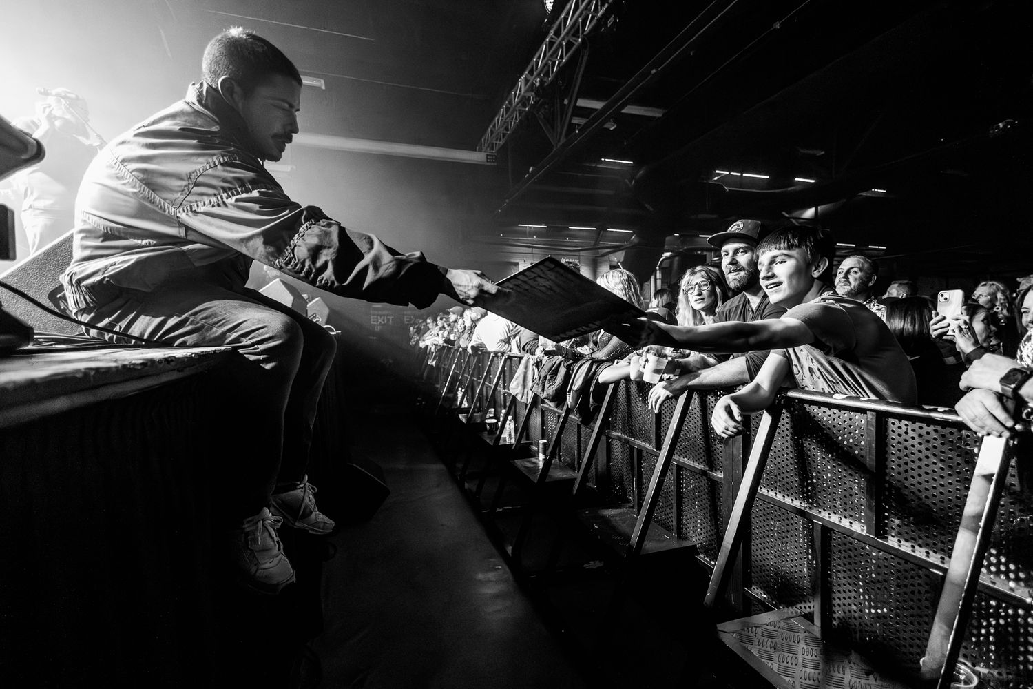 Dramatic black and white photo of stage performer reaching out to audience behind barrier.