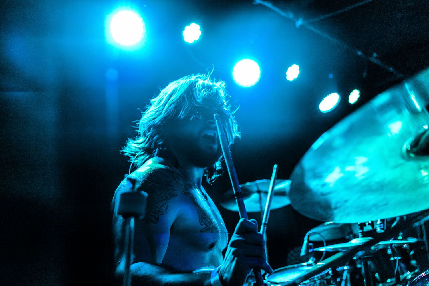 Silhouetted drummer performing on stage with dramatic blue spotlights.