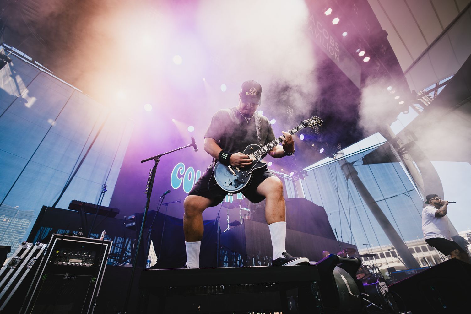 Musician playing electric guitar while seated on stage with purple atmospheric lighting.