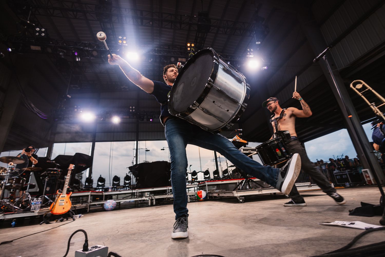 Musicians performing with high energy on stage while holding drum equipment.