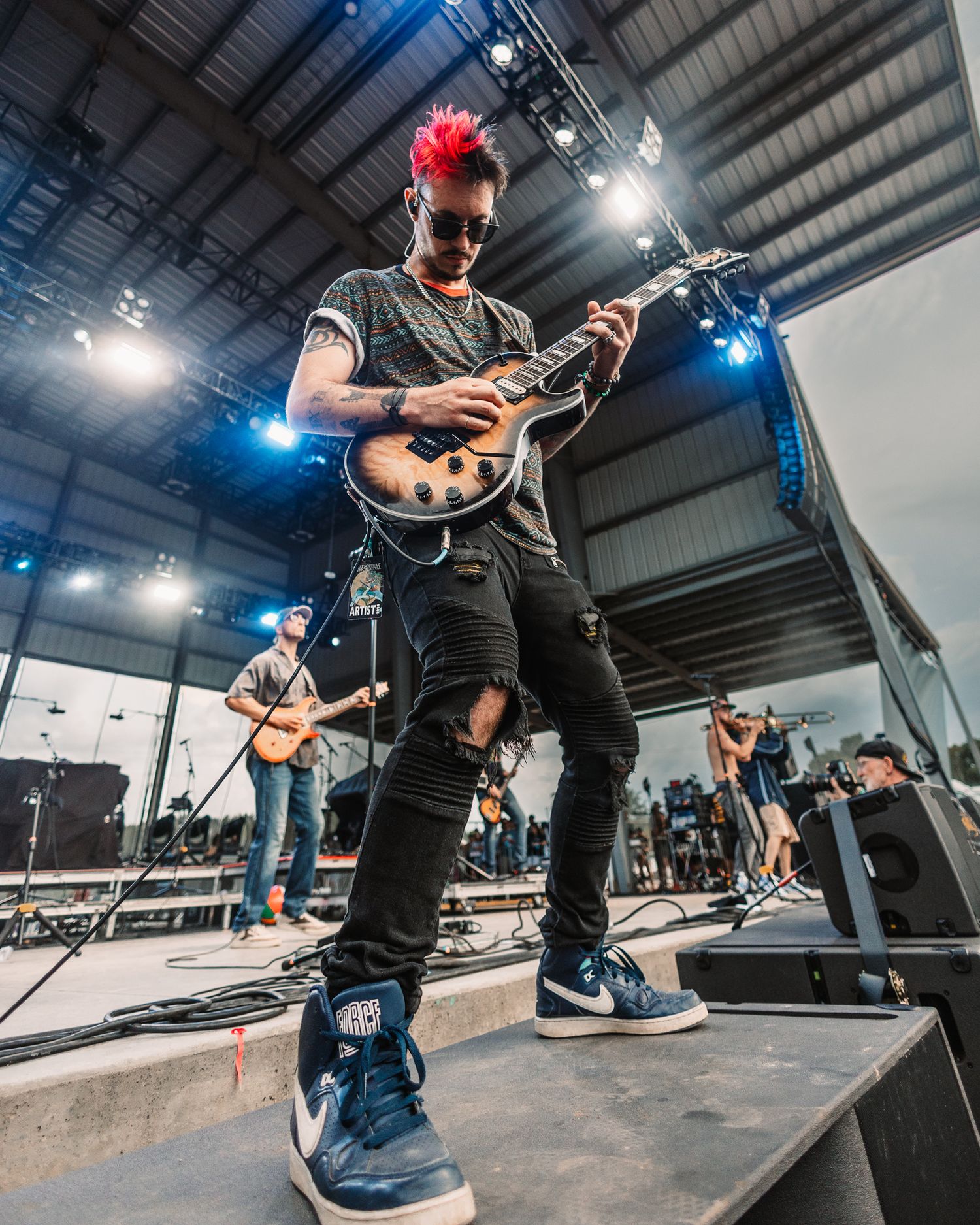 Guitarist with red mohawk performs on stage with professional lighting.