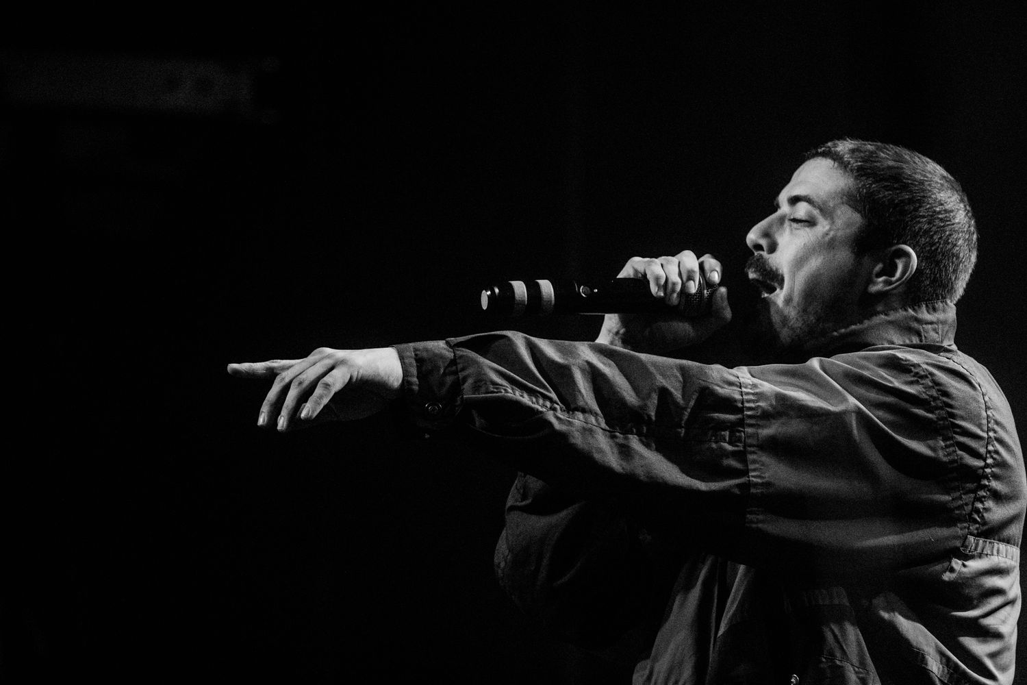 Black and white shot of a performer gesturing dramatically while singing on stage.