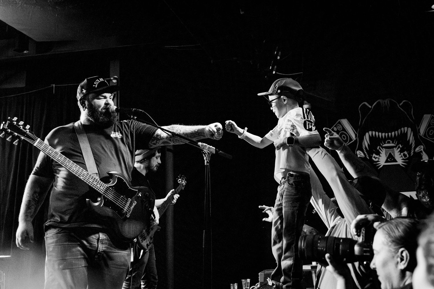 Musicians performing on stage during energetic live concert in black and white.