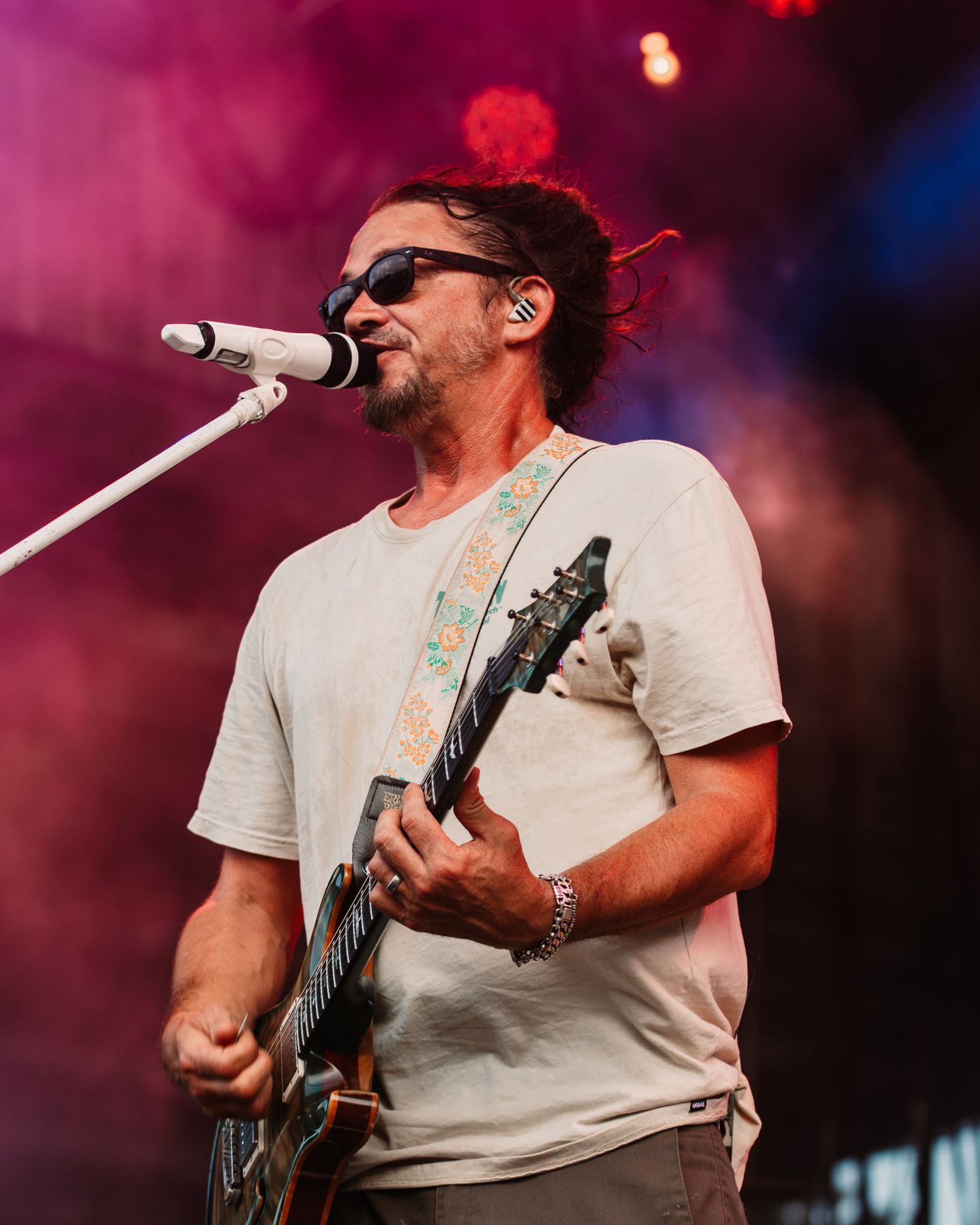 Energetic musician plays guitar during a vibrant outdoor performance with pink lighting effects.