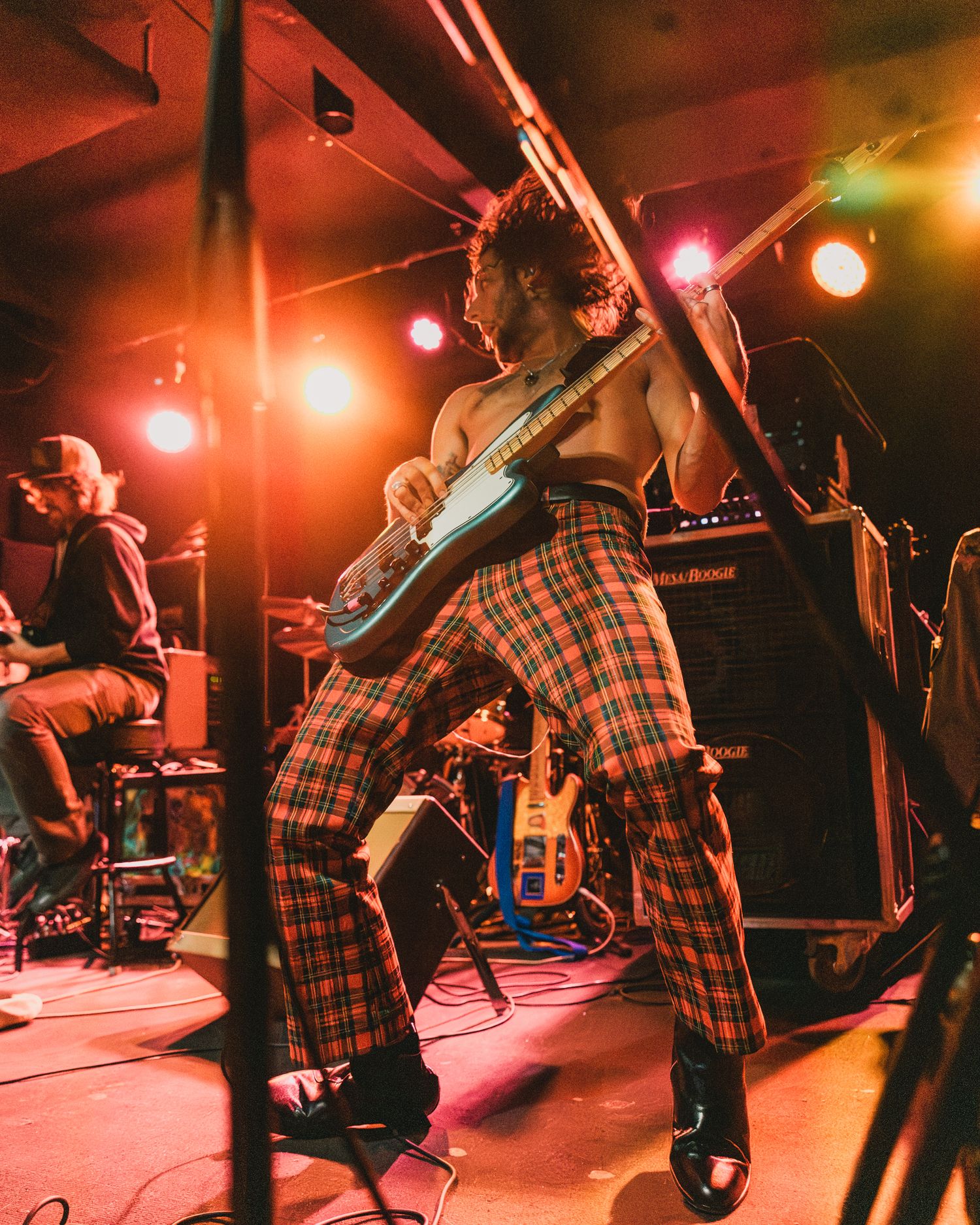 Musician in plaid pants playing guitar during energetic stage performance.