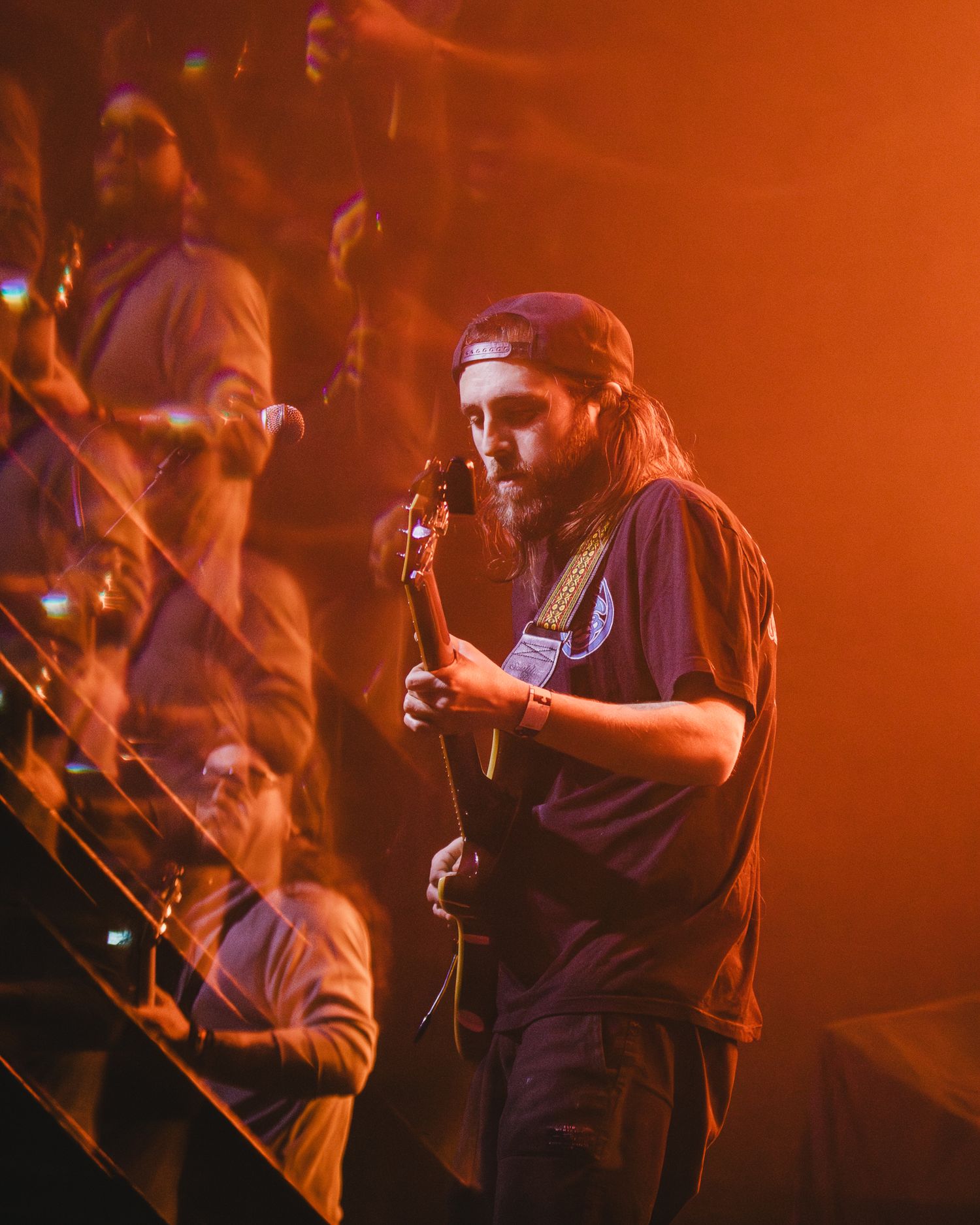 Performer plays guitar under orange stage lights during concert.