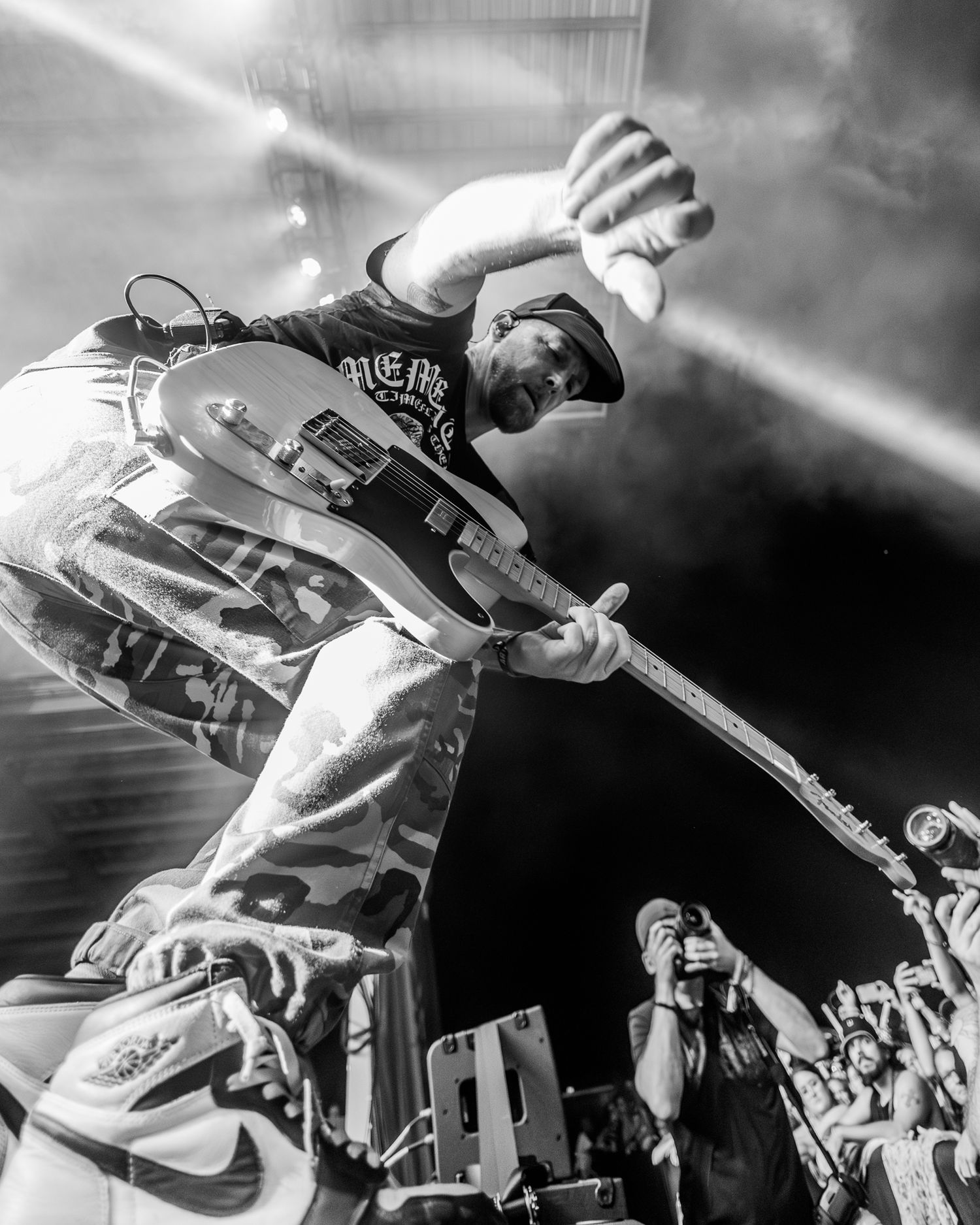 Dynamic black and white shot of guitarist performing acrobatic jump move during concert performance.