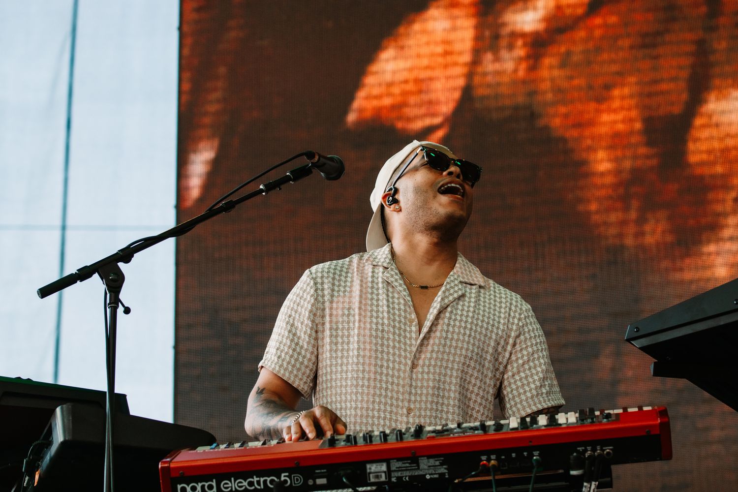 Musician playing red keyboard on outdoor festival stage during daytime performance.