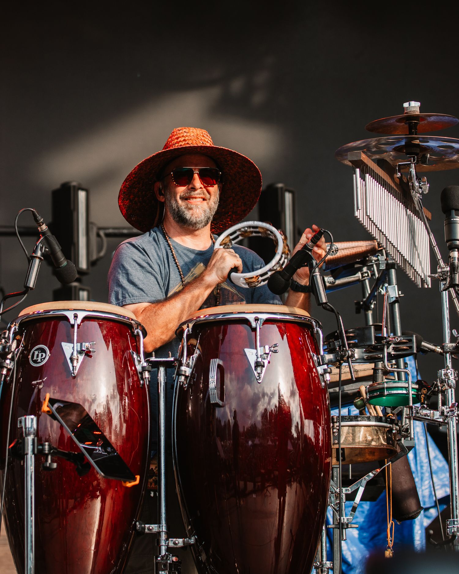 Musician in orange hat plays red conga drums on stage during live performance.