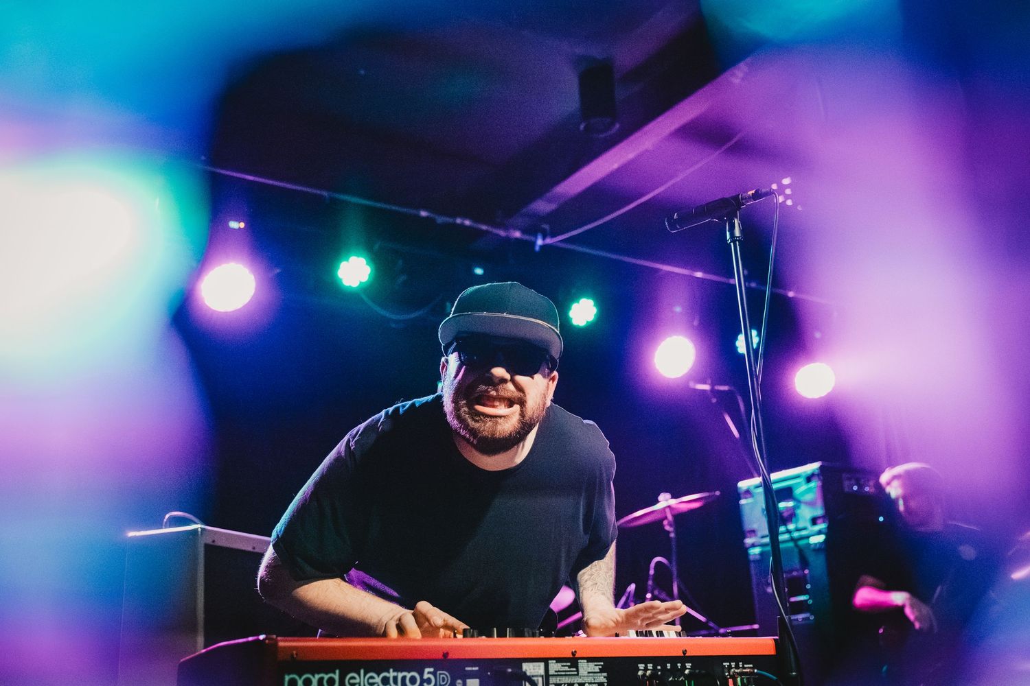 Musician playing keyboard on stage with colorful purple and blue lighting effects.