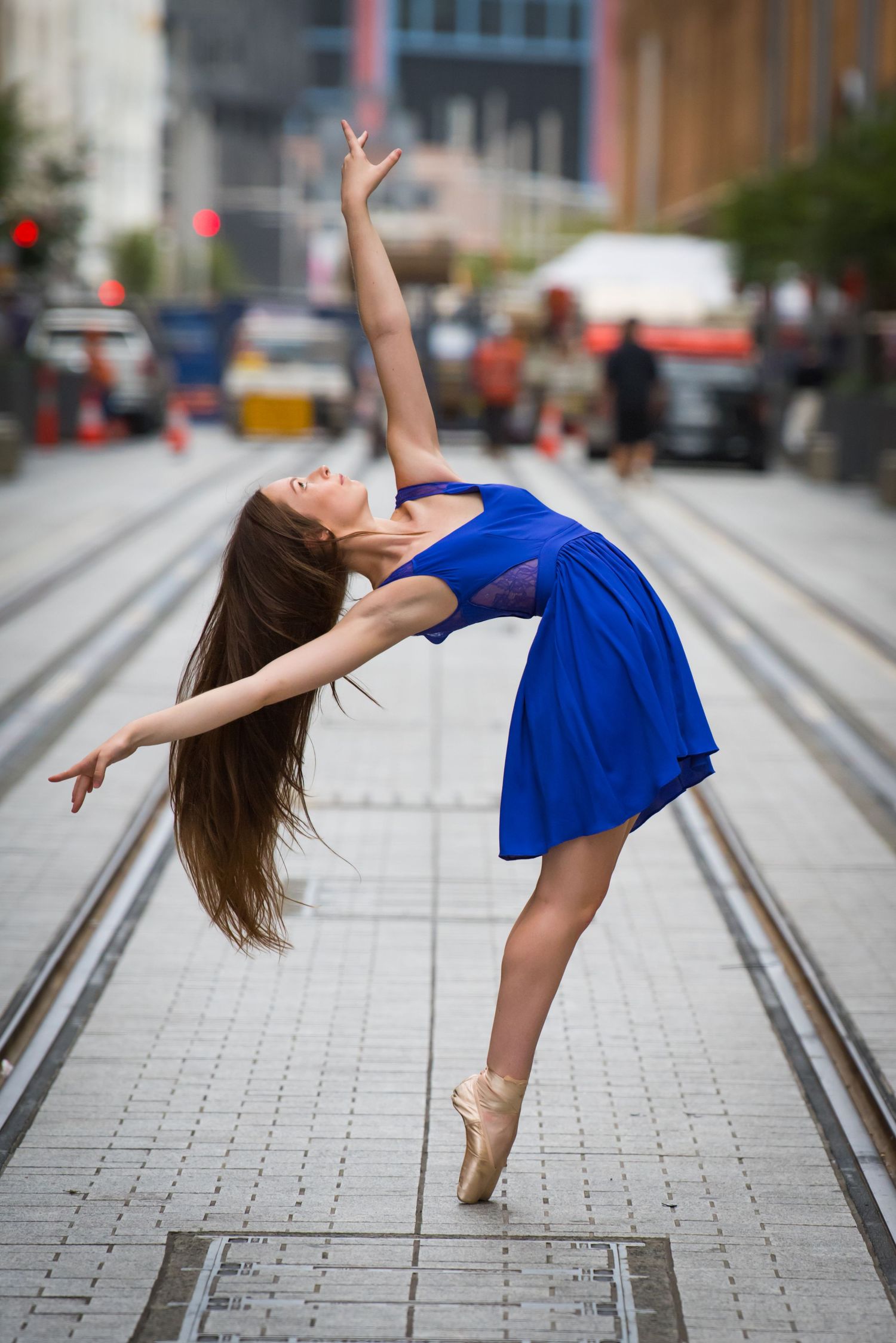 Ballet dancer in blue dress performs graceful arabesque on urban sidewalk.