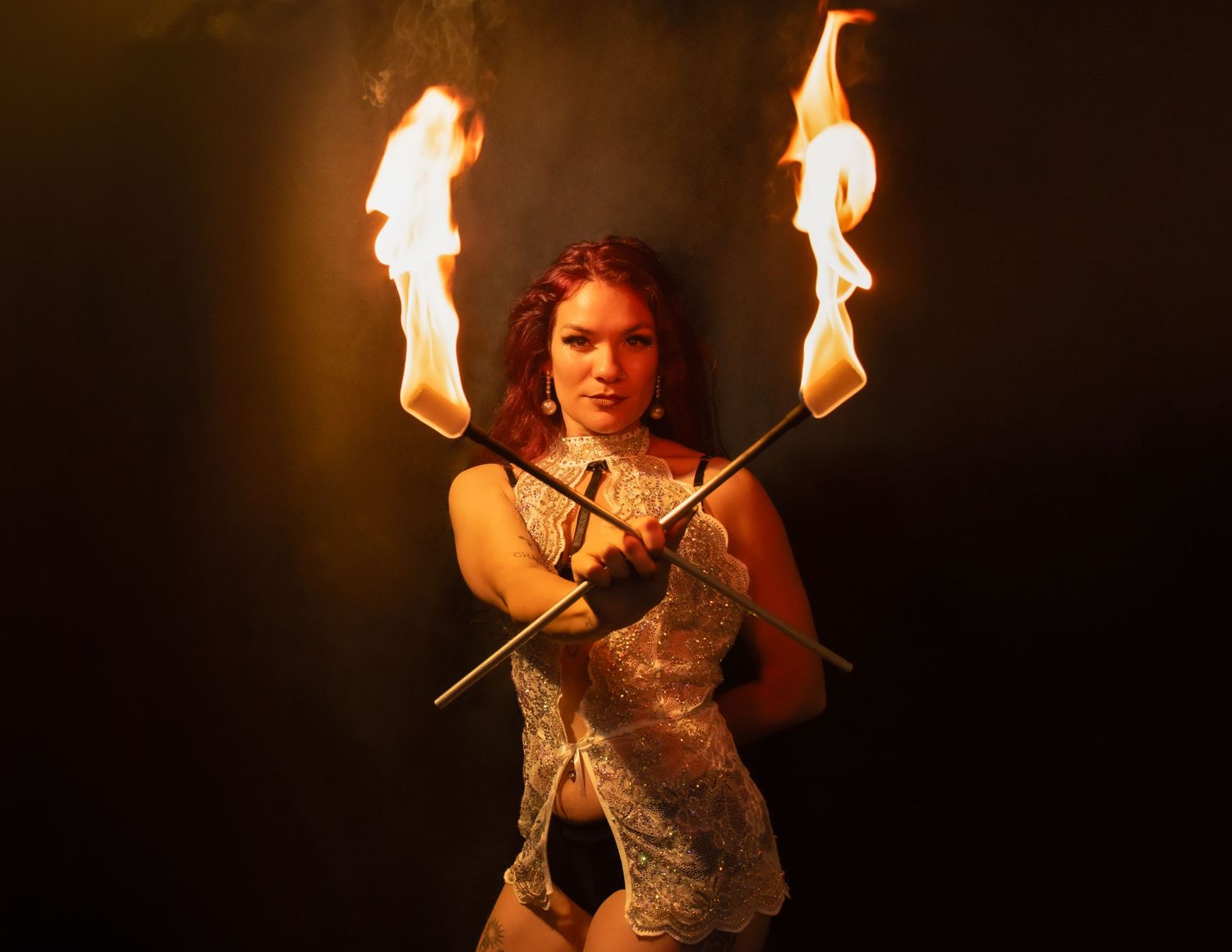 Fire artist creates mesmerizing patterns with dual flaming torches in dark setting.