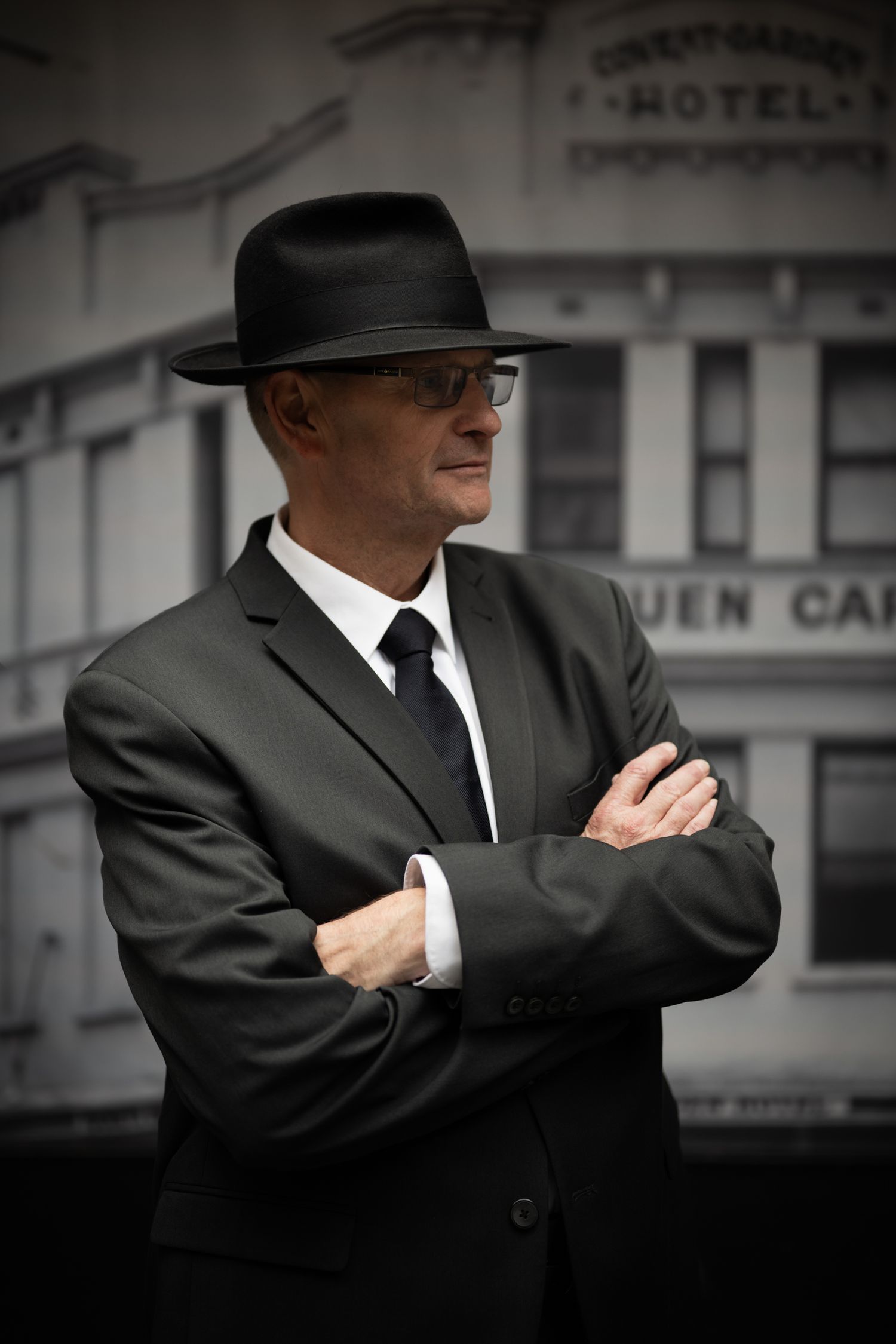 Mysterious figures in suits and hats create film noir style poses in black and white.