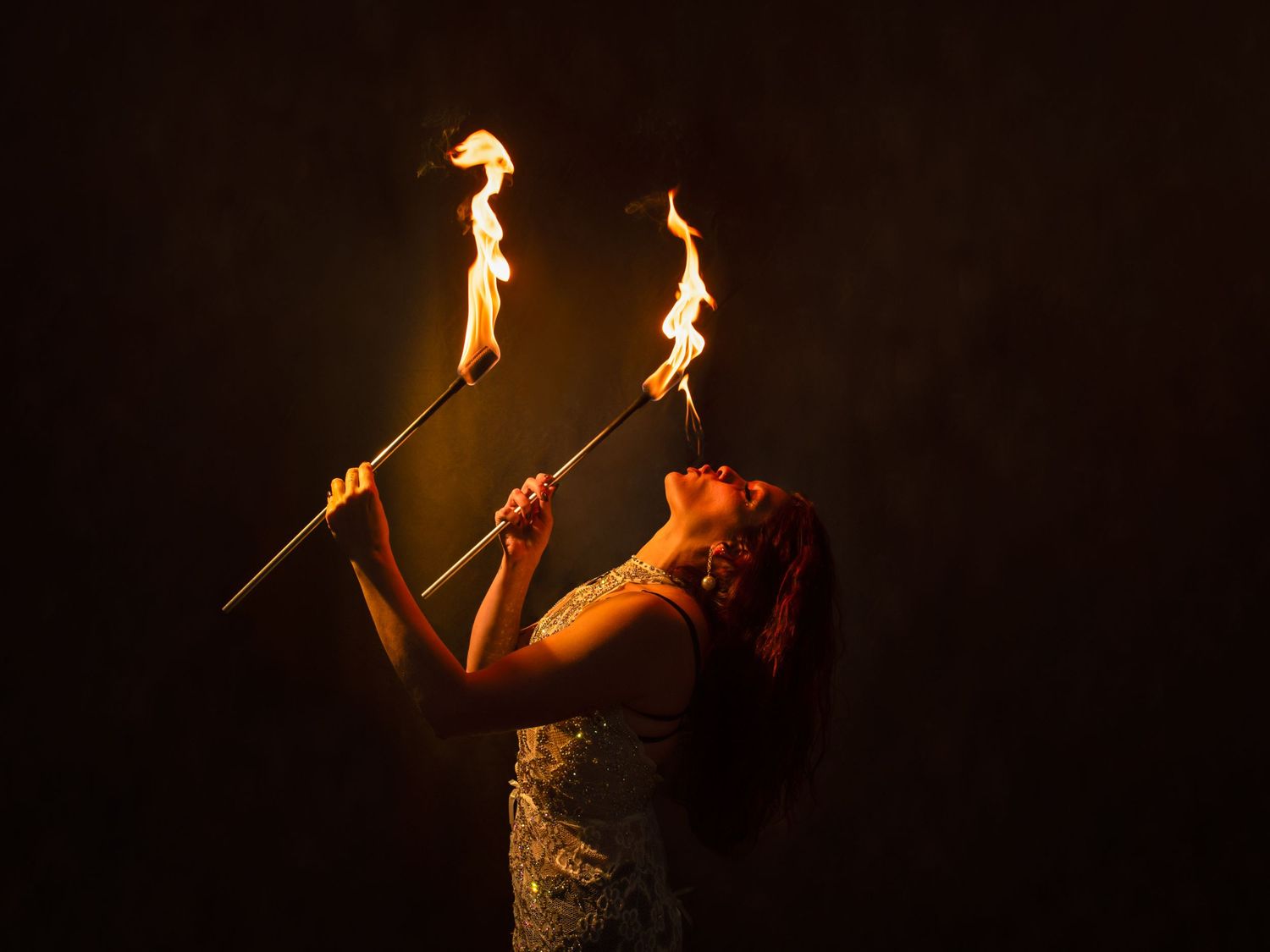 Fire performer creates dramatic shapes with flaming batons in theatrical lighting.