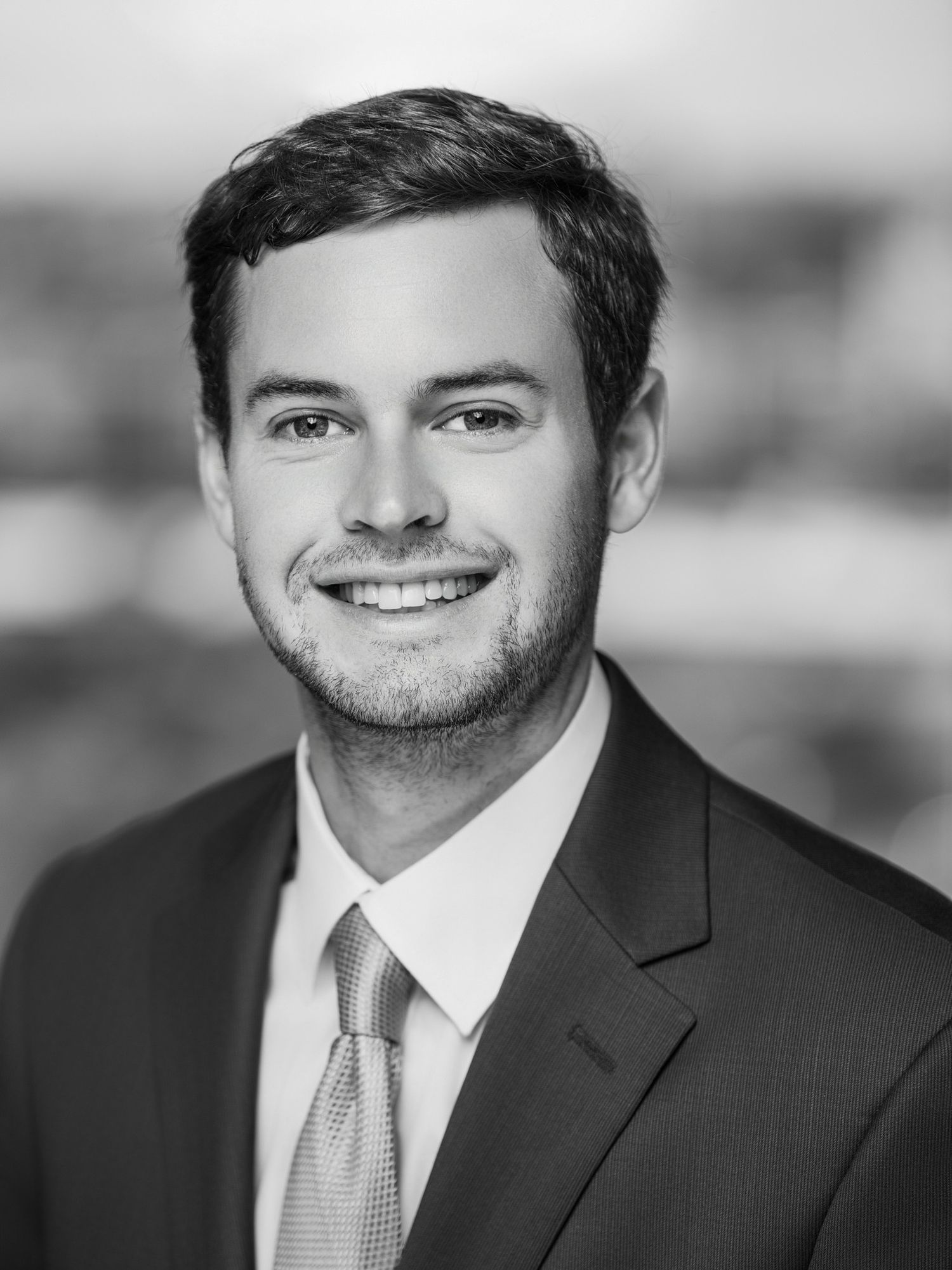 Black and white business portrait of person in suit and tie with confident smile.