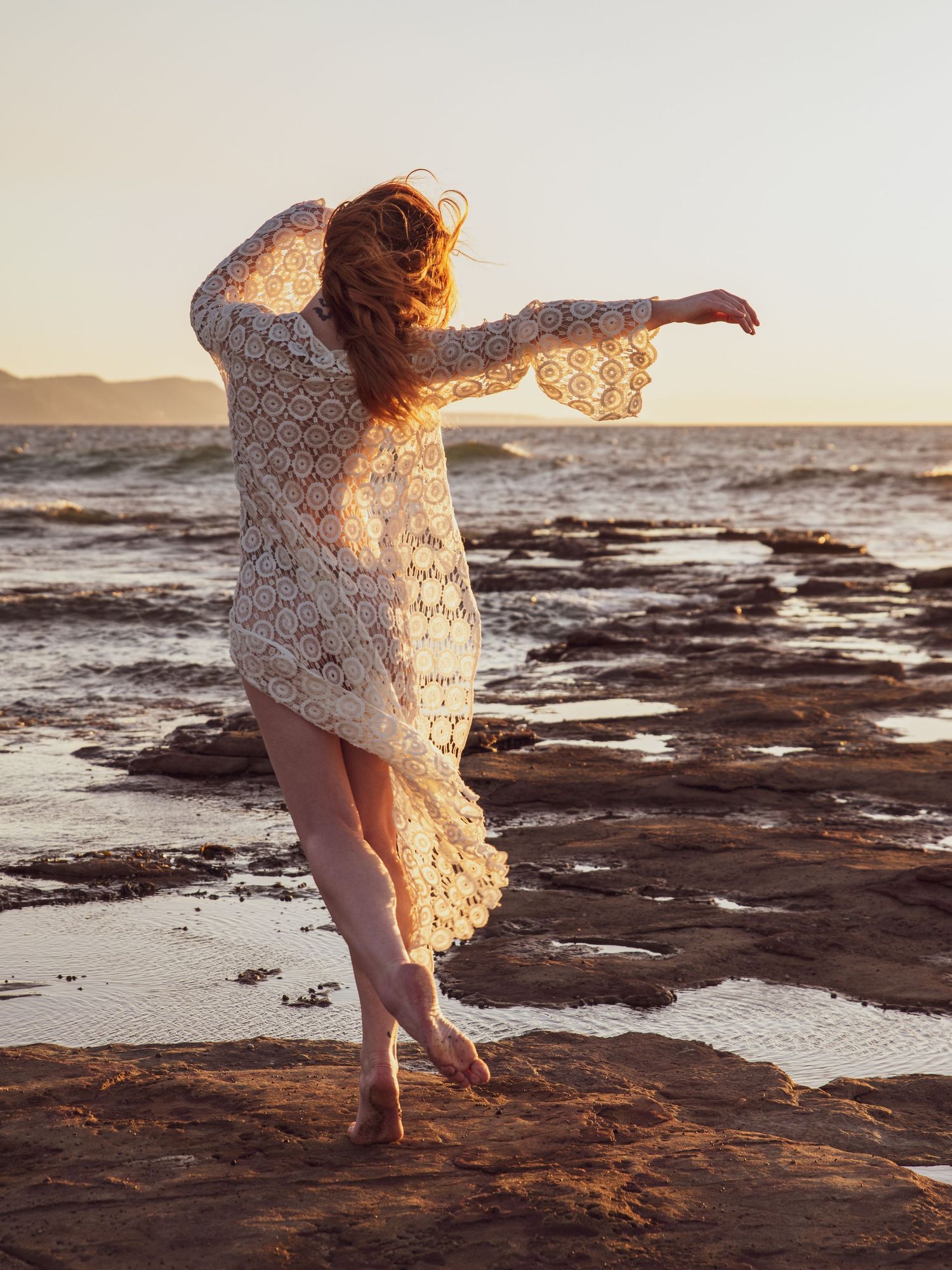 Ethereal beach photoshoot with flowing white dress at sunset.