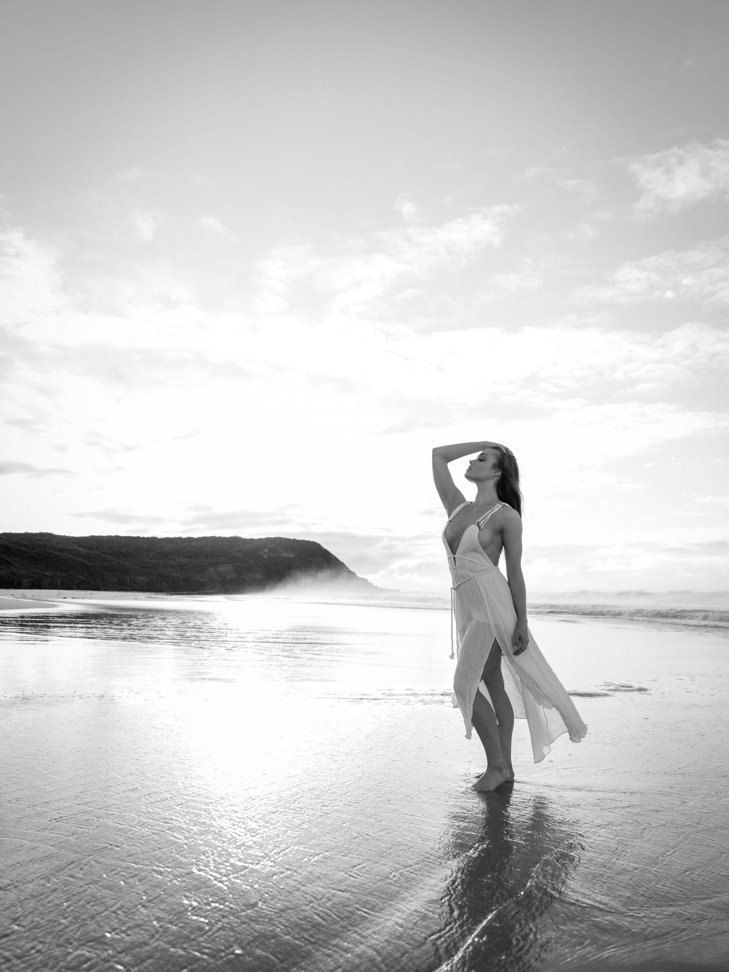 Silhouetted dancer poses gracefully on a misty beach at sunset.