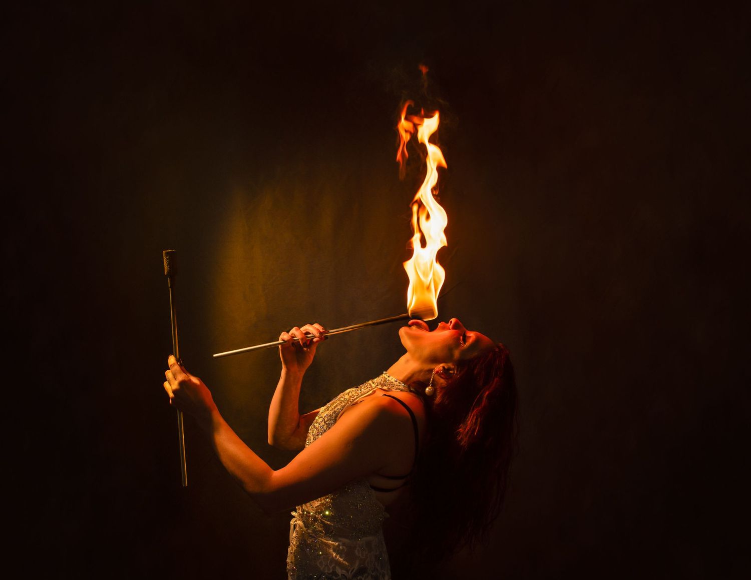 Performer spins flaming batons in dramatic fire dance routine against black background.
