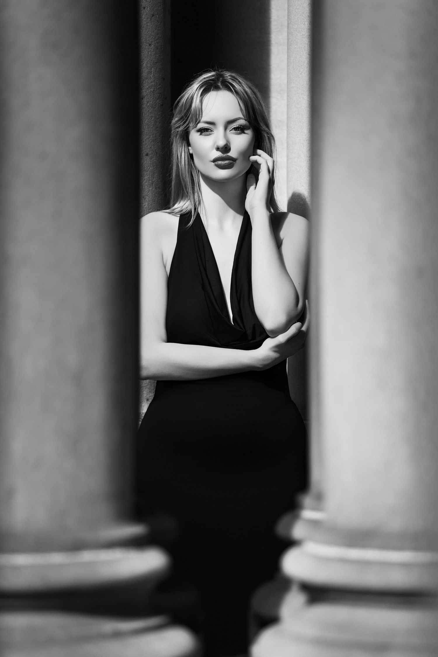 Artistic black and white portrait with architectural columns creating dramatic shadows.