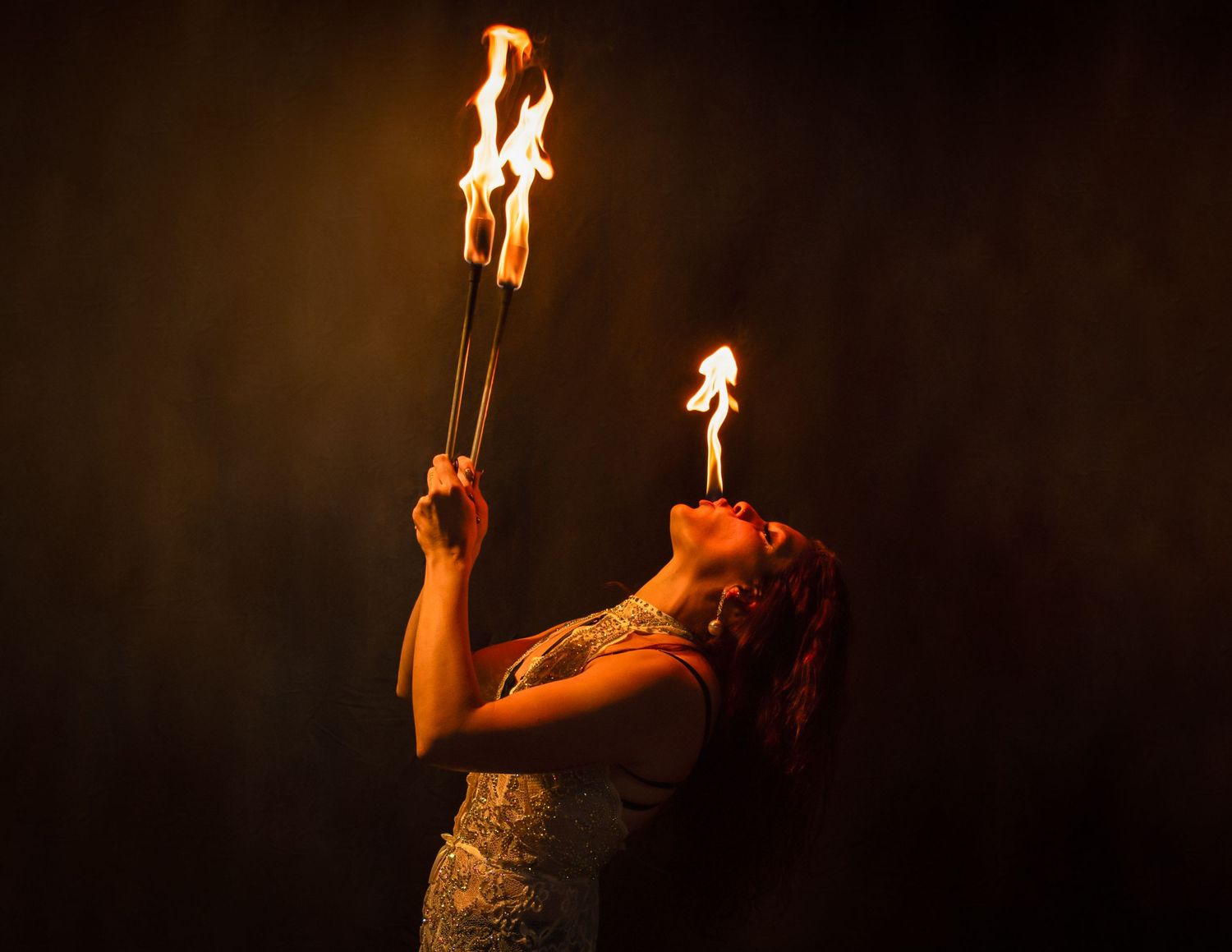 Artist performs dramatic fire dance routine with flaming props in darkened studio setting.