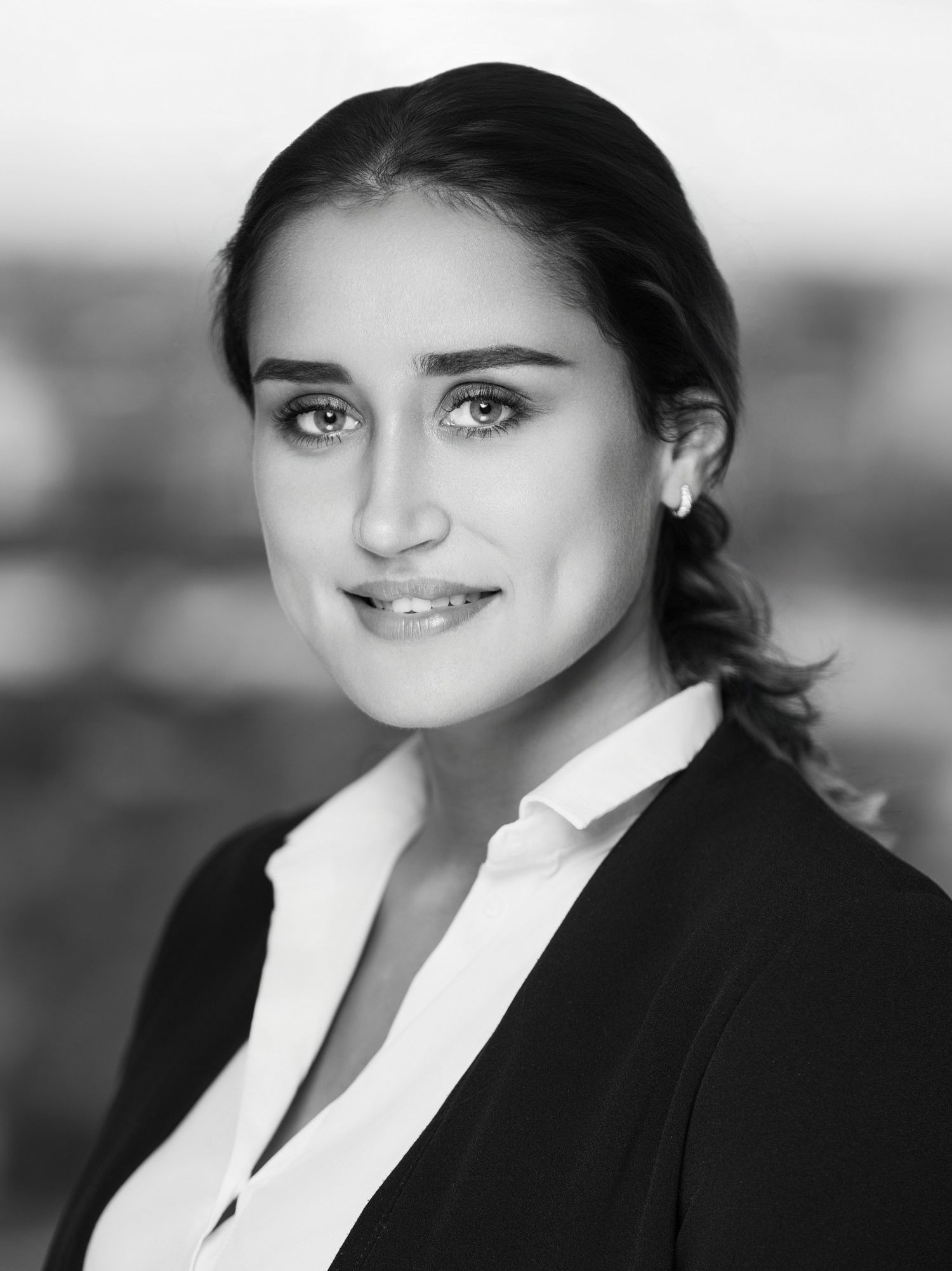 Professional headshot of person in dark blazer and white blouse against light backdrop.