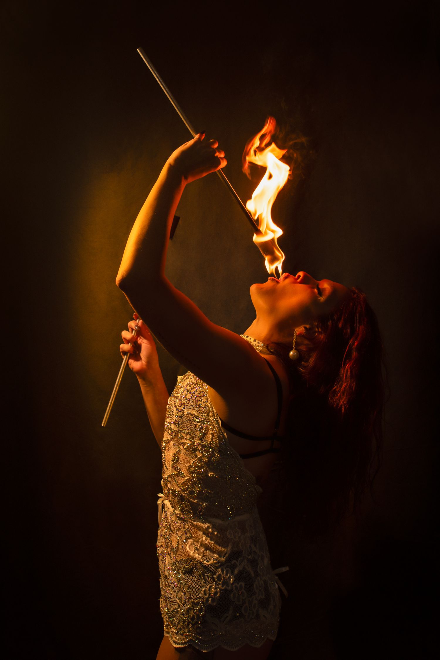 Fire dancer manipulates burning batons in artistic performance against black backdrop.