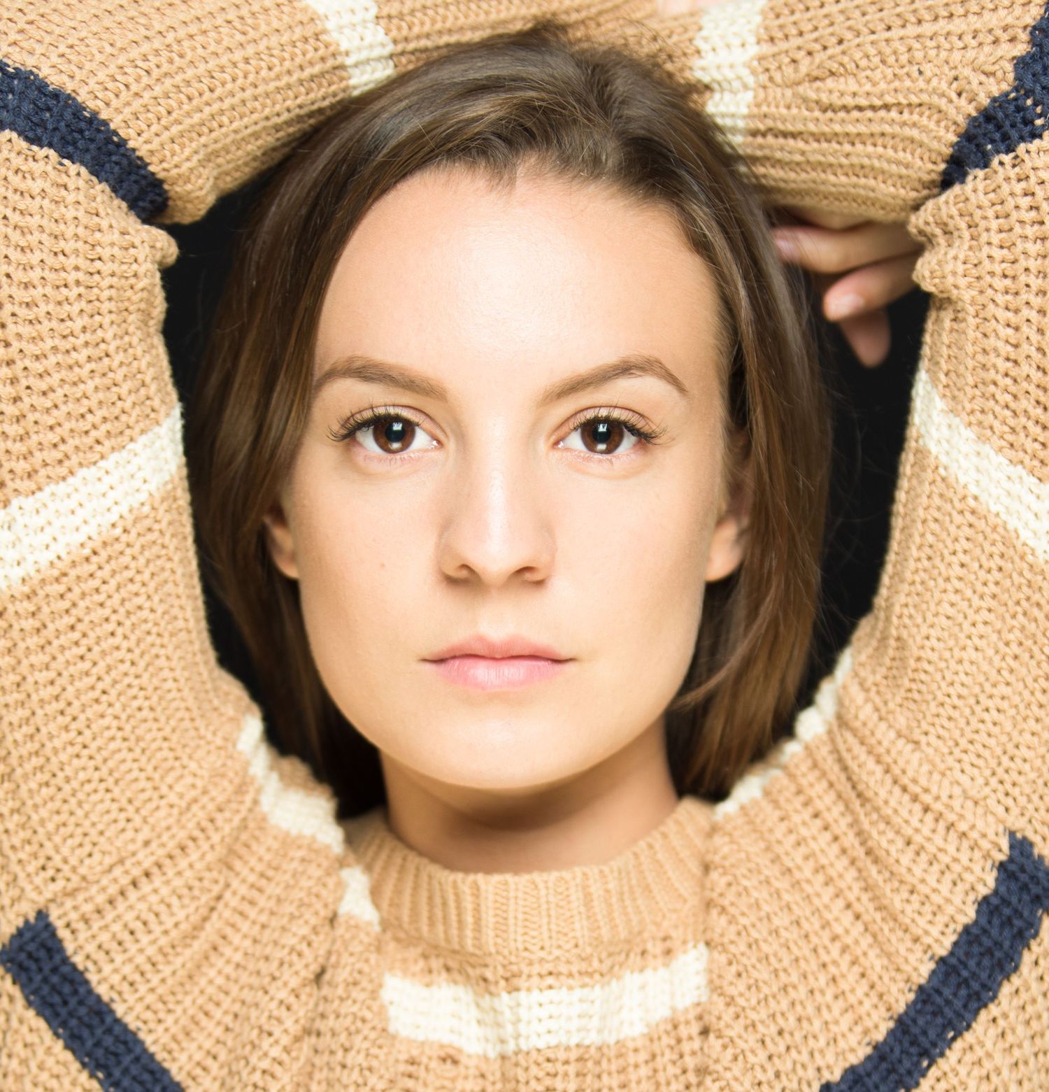 Close-up artistic portrait with a beige knit sweater frame against white background.