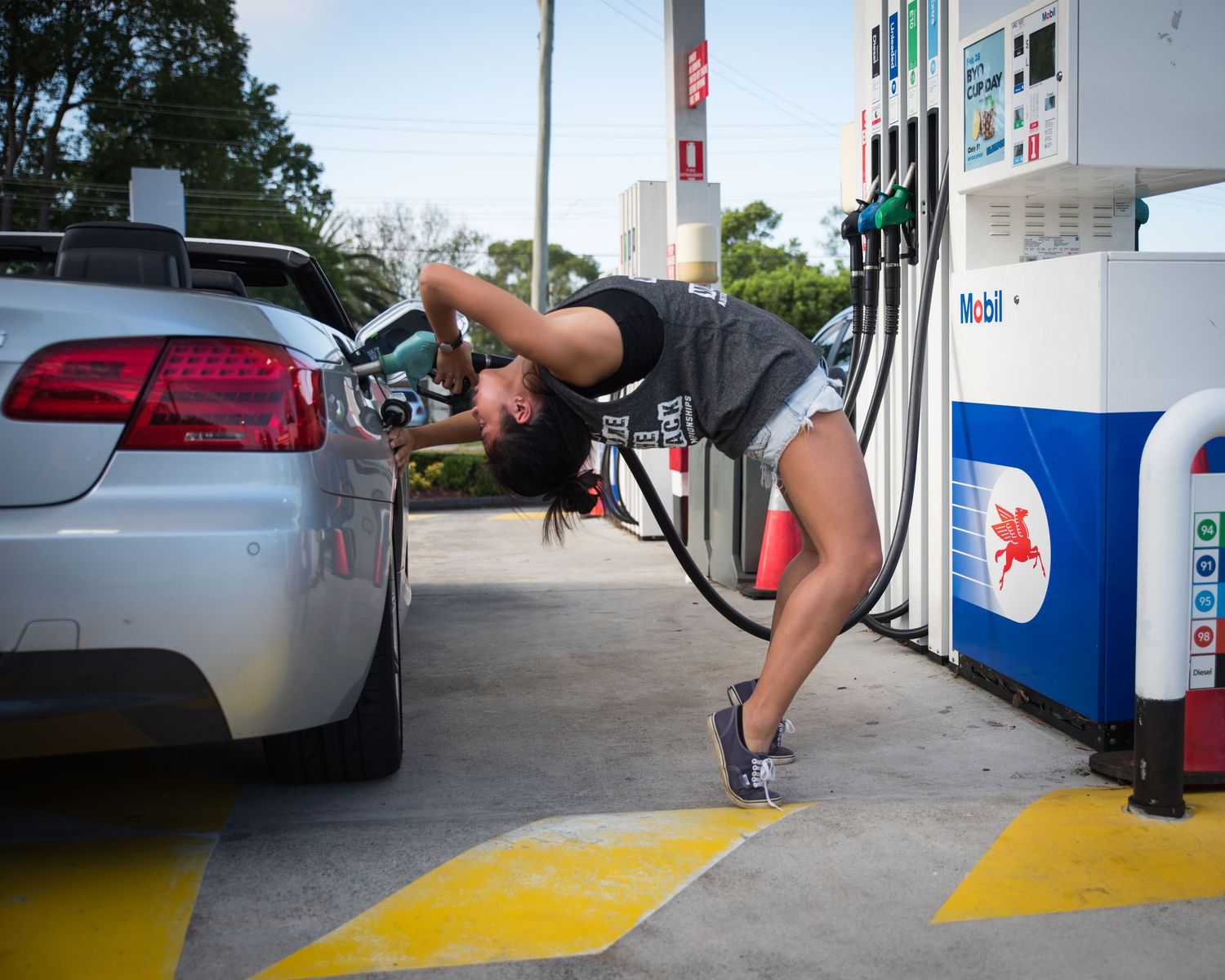 Athletic figure demonstrates flexible poses at gas station pump.