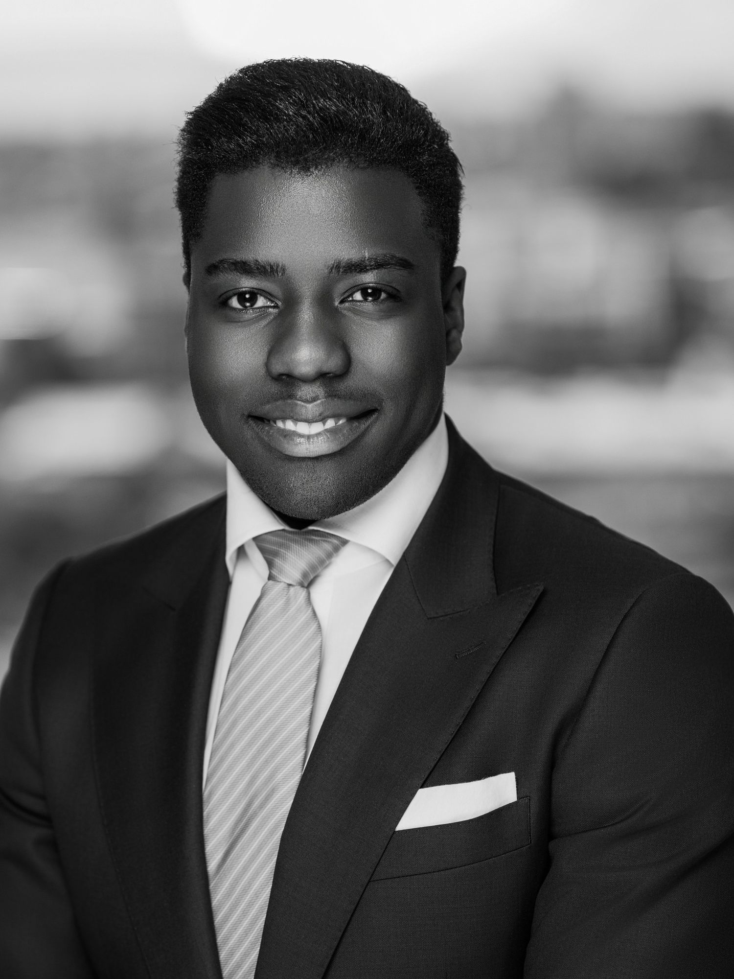 Black and white portrait of person in formal suit with striped tie and pocket square.