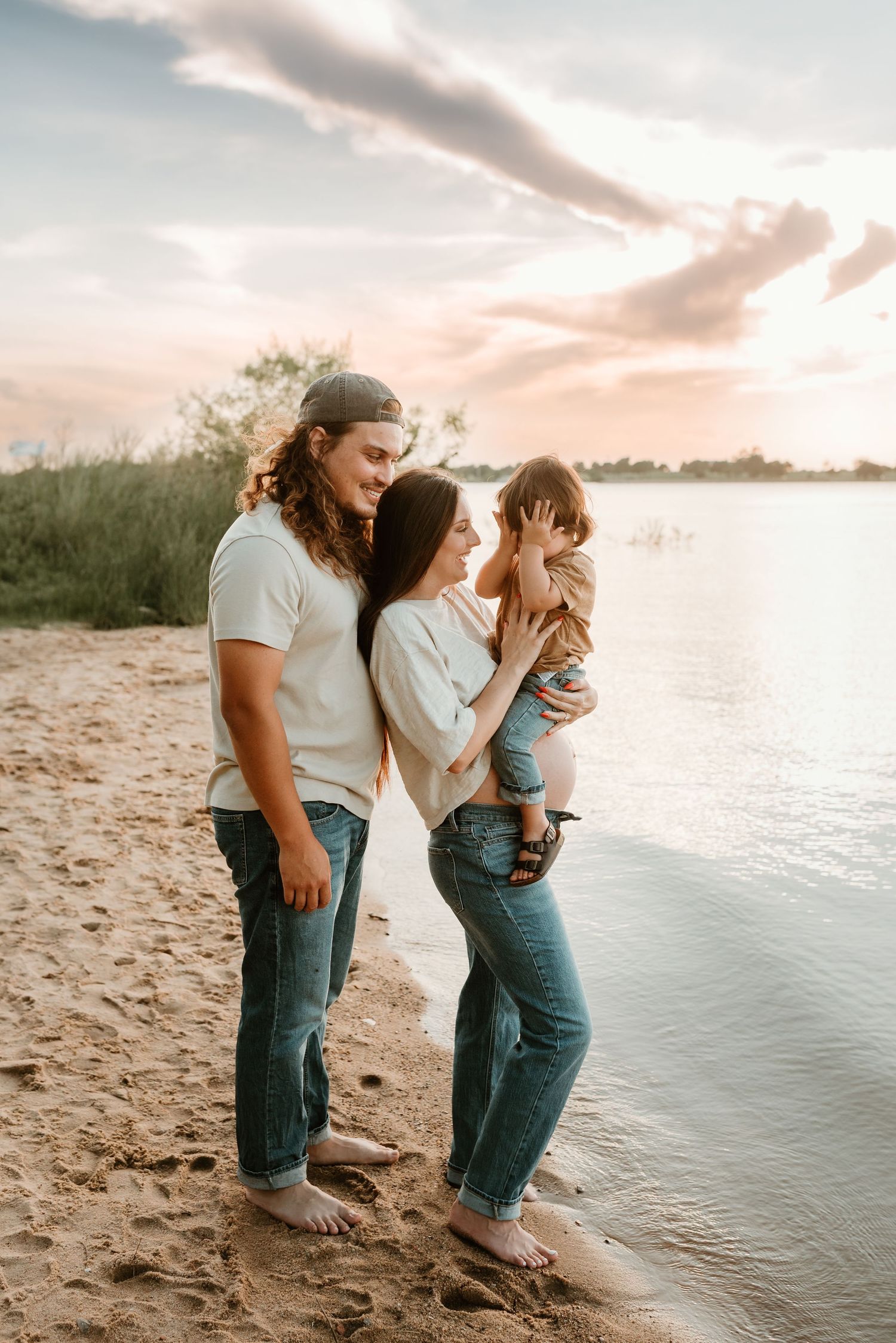 Young family of three shares a tender moment on a sandy beach at golden sunset.