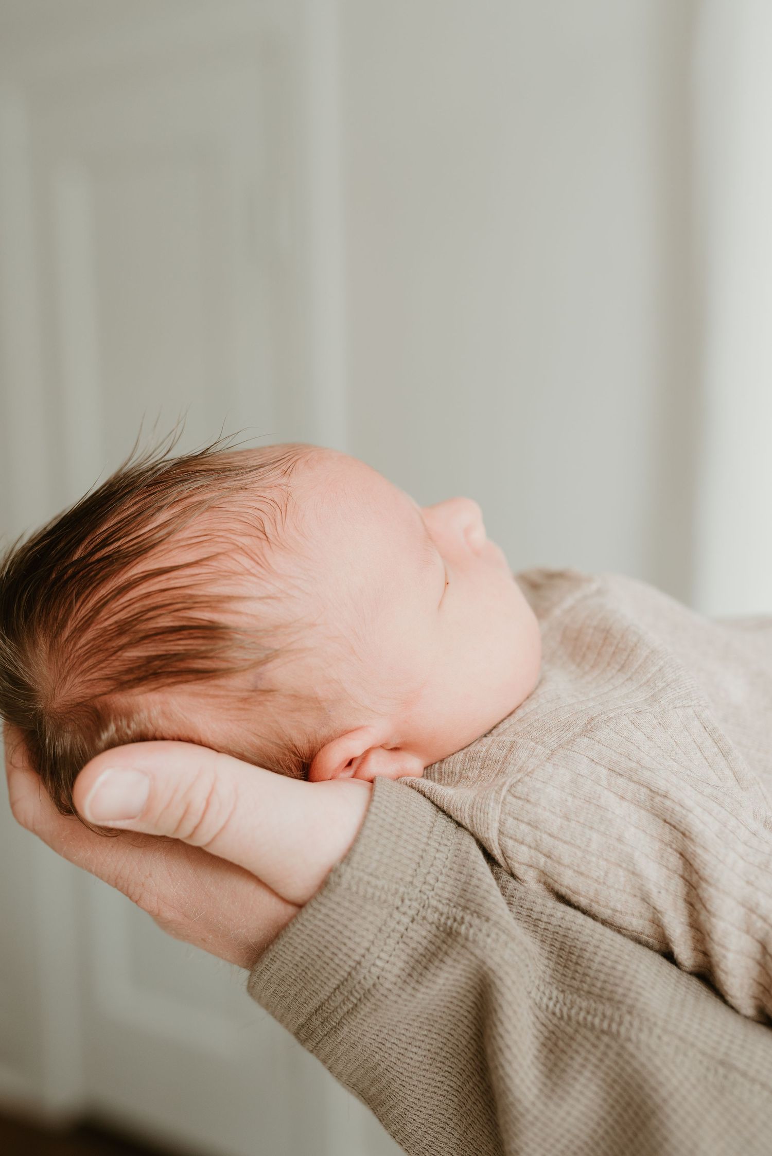 Peaceful newborn baby sleeping soundly in a parent's gentle supporting hand.