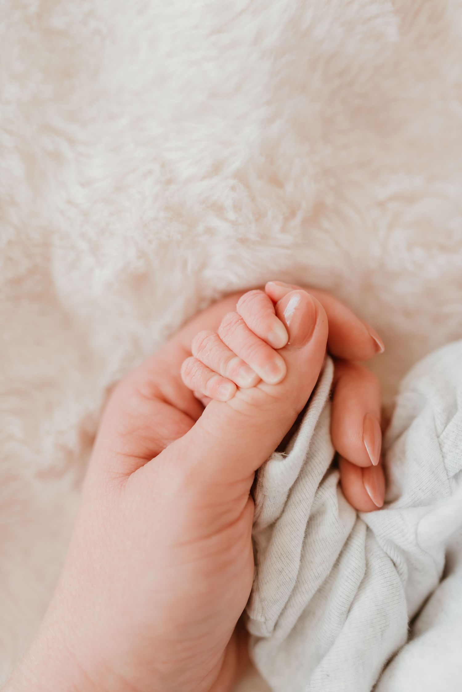 Tiny newborn baby hand gently grasping mother's finger on a soft white fluffy blanket.