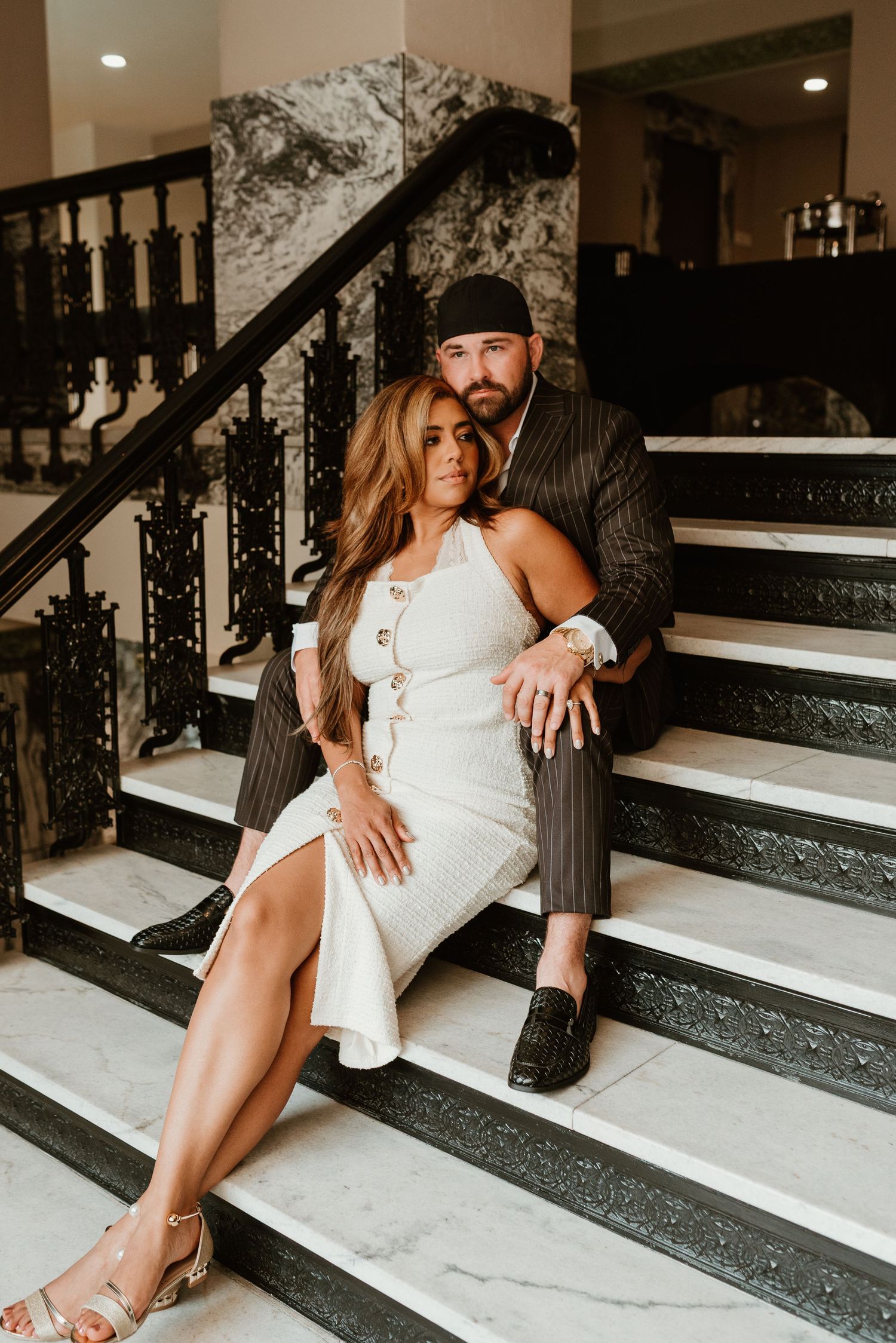 Stylish couple sitting on marble stairs in an elegant venue interior.