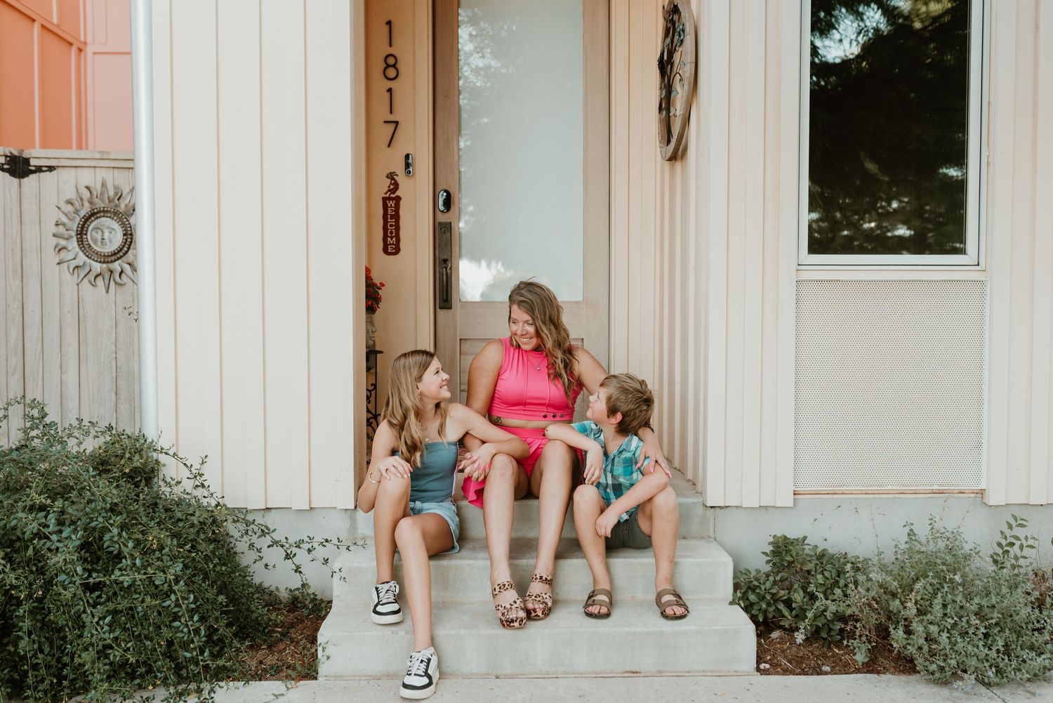 Mother sitting on front porch steps with her two young children on a sunny day.