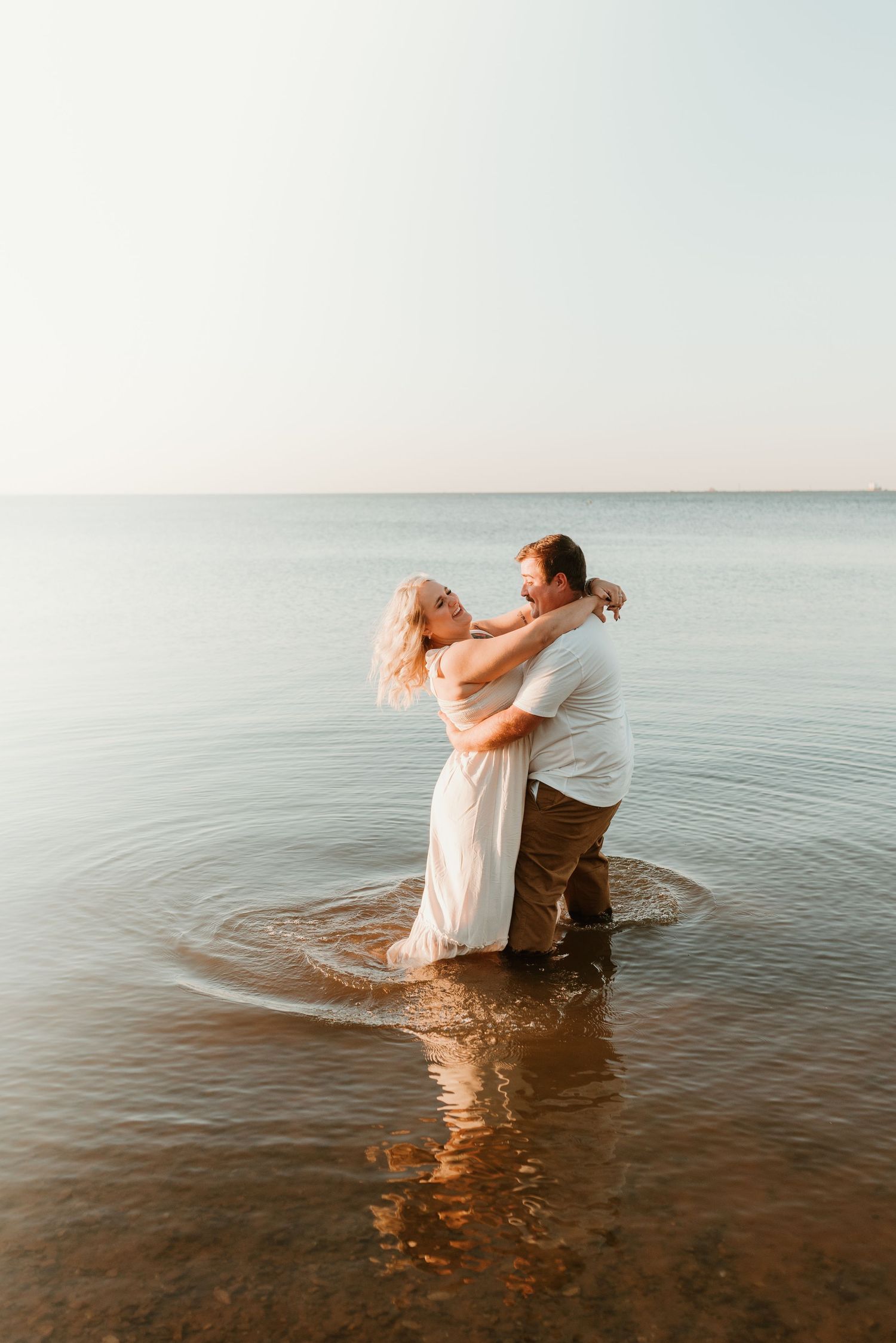 Romantic couple embracing while standing in shallow lake water at sunset.