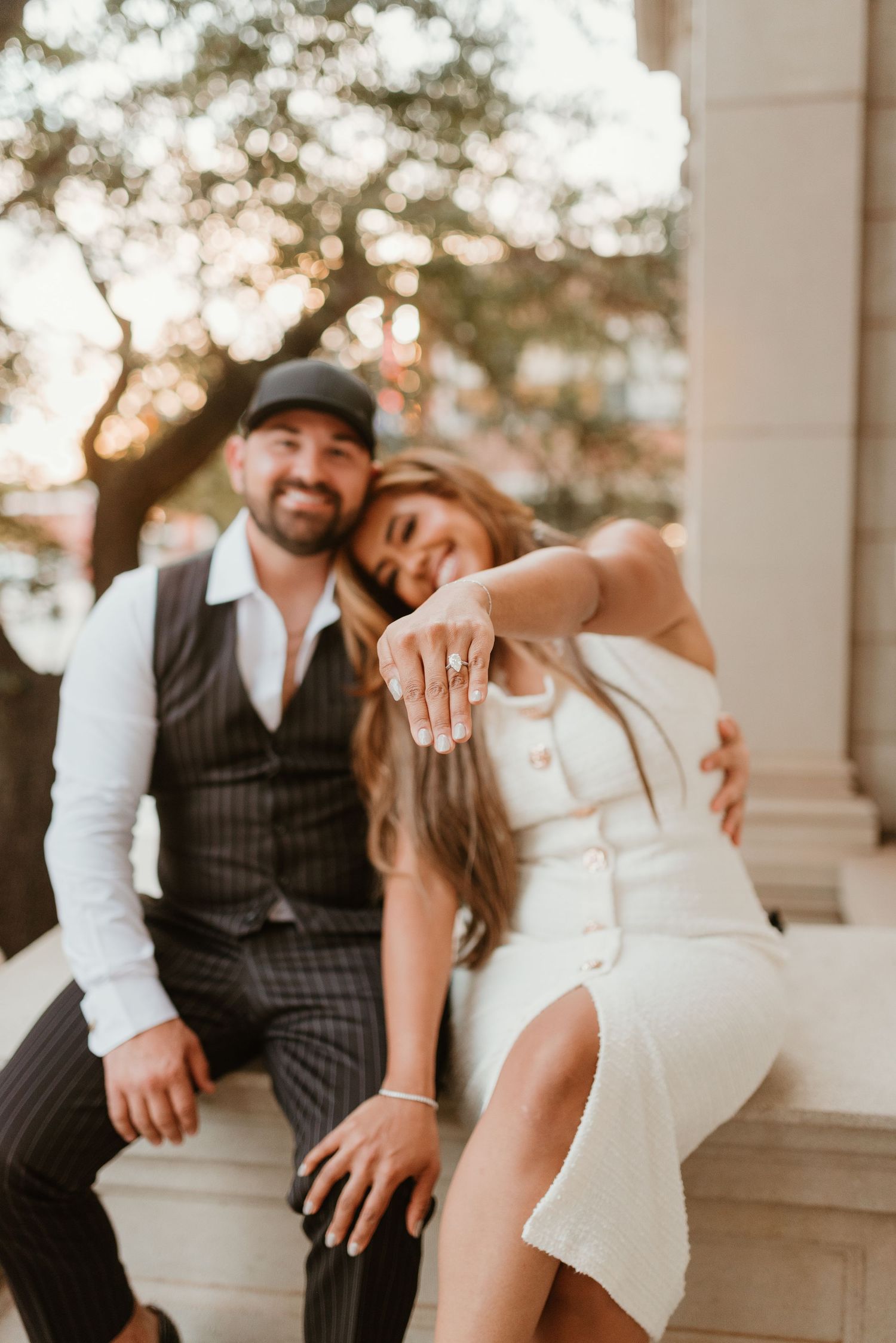 Engaged couple smiling and showing off diamond engagement ring outdoors.