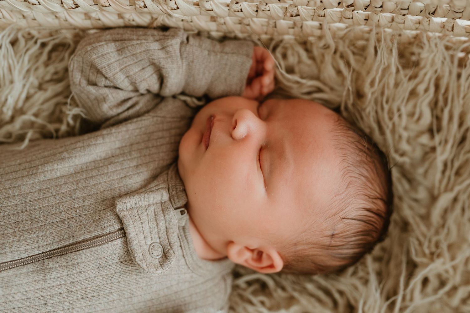 A serene newborn baby sleeps peacefully in a beige knit romper on a soft textured blanket.