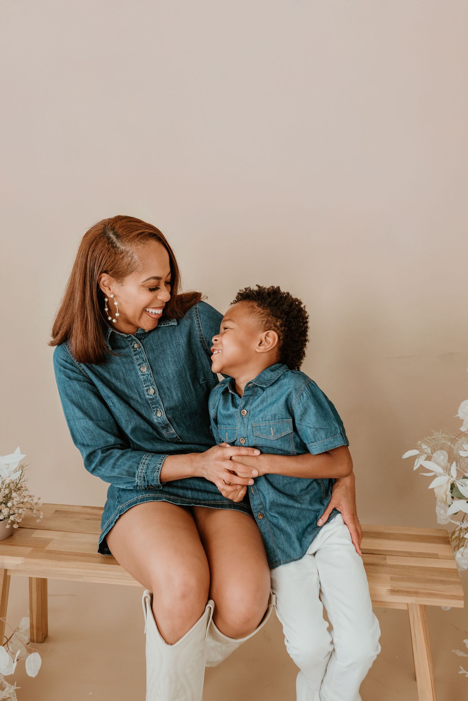 Mother and young son in matching denim outfits share a joyful moment on a wooden bench.