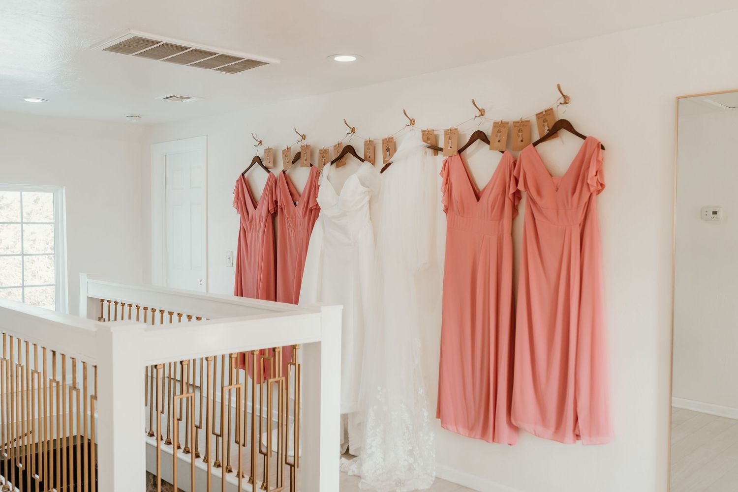 Coral bridesmaid dresses and white wedding gown hanging on antler hooks along a staircase wall.