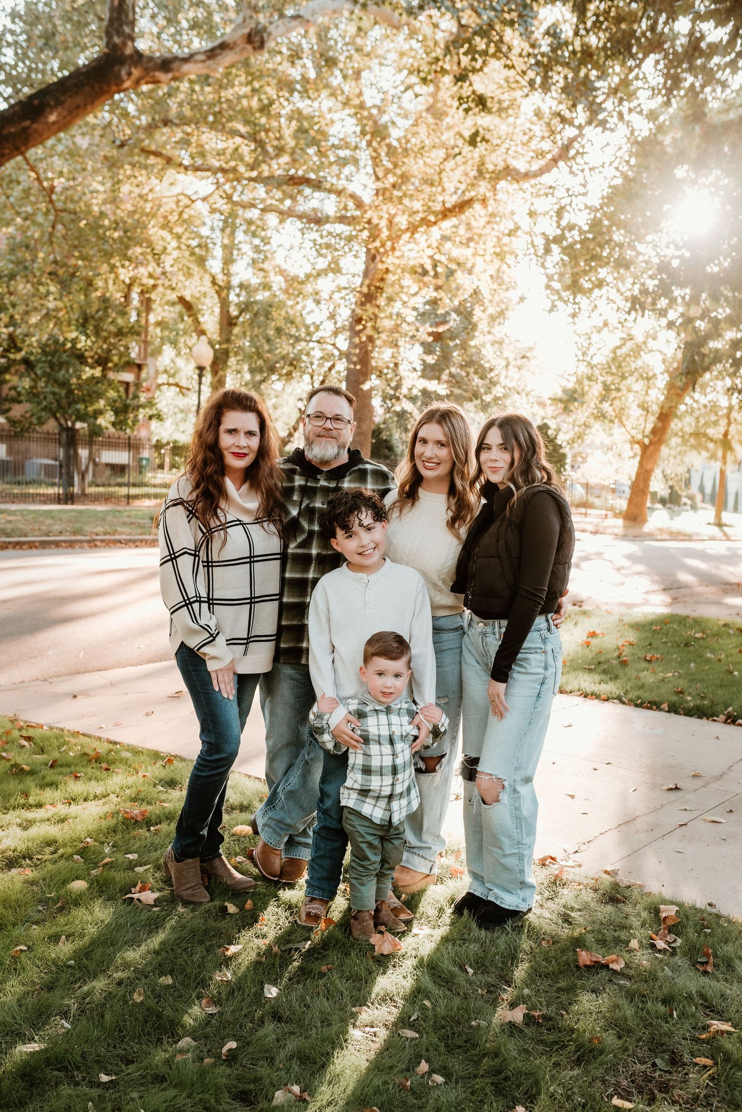 Extended family of six poses on sunny tree-lined sidewalk during fall outdoor portrait session.