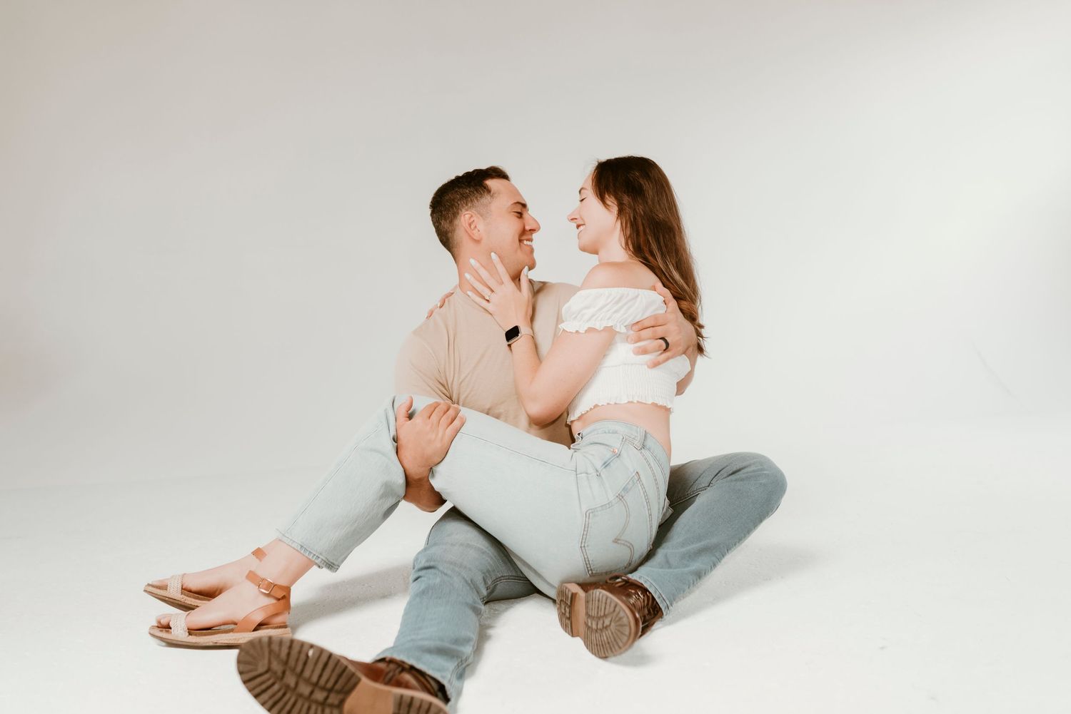 Couple sitting on floor gazing at each other lovingly in a bright studio photo session.