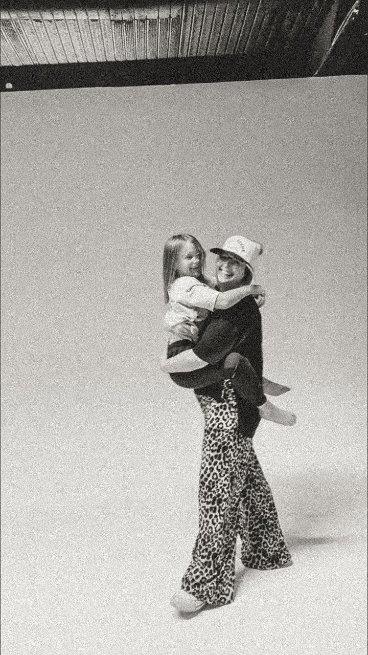Black and white photo of a woman in leopard print flared pants holding a young child in an open studio space.