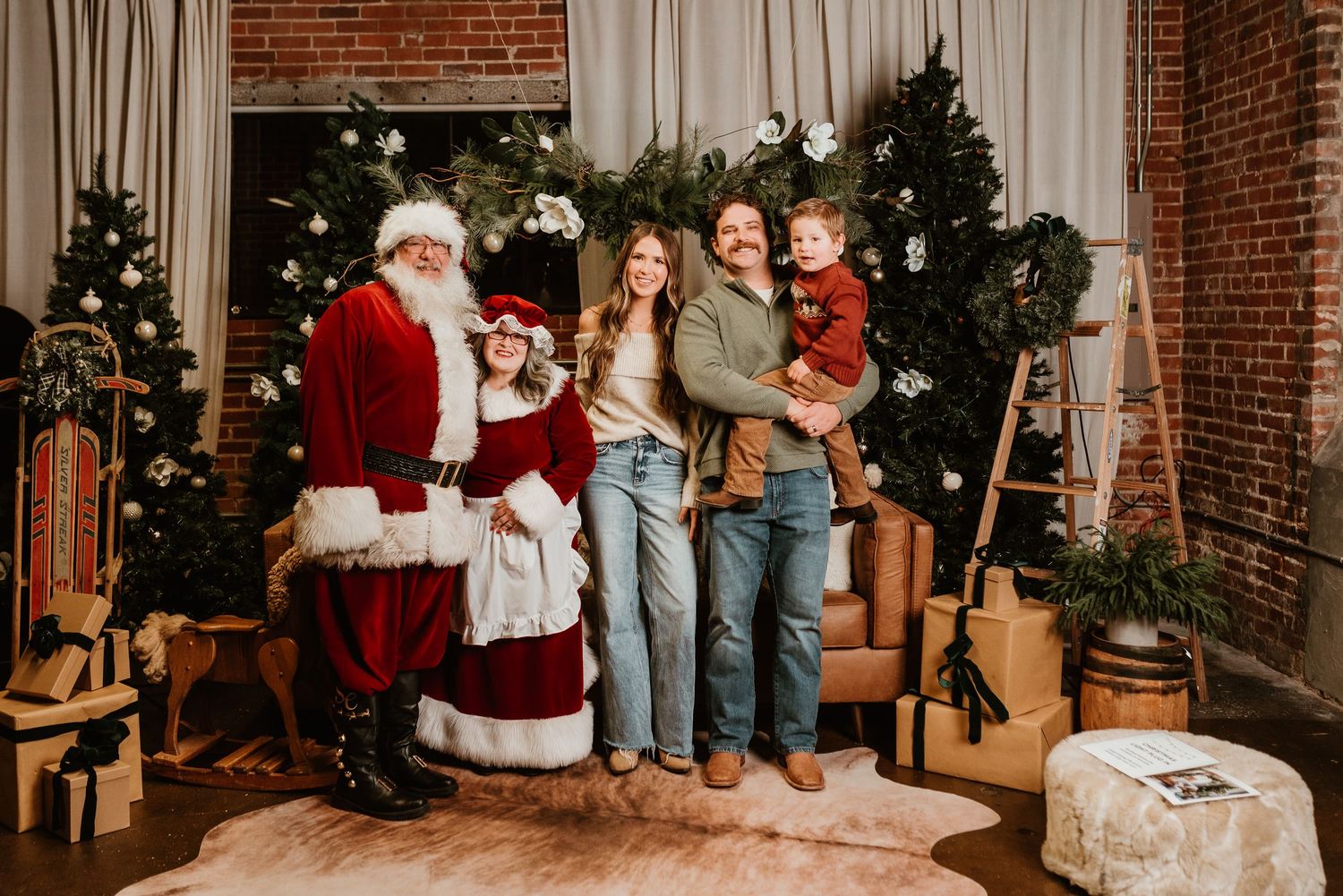 A family poses with Santa and Mrs. Claus in a festively decorated Christmas studio setting.