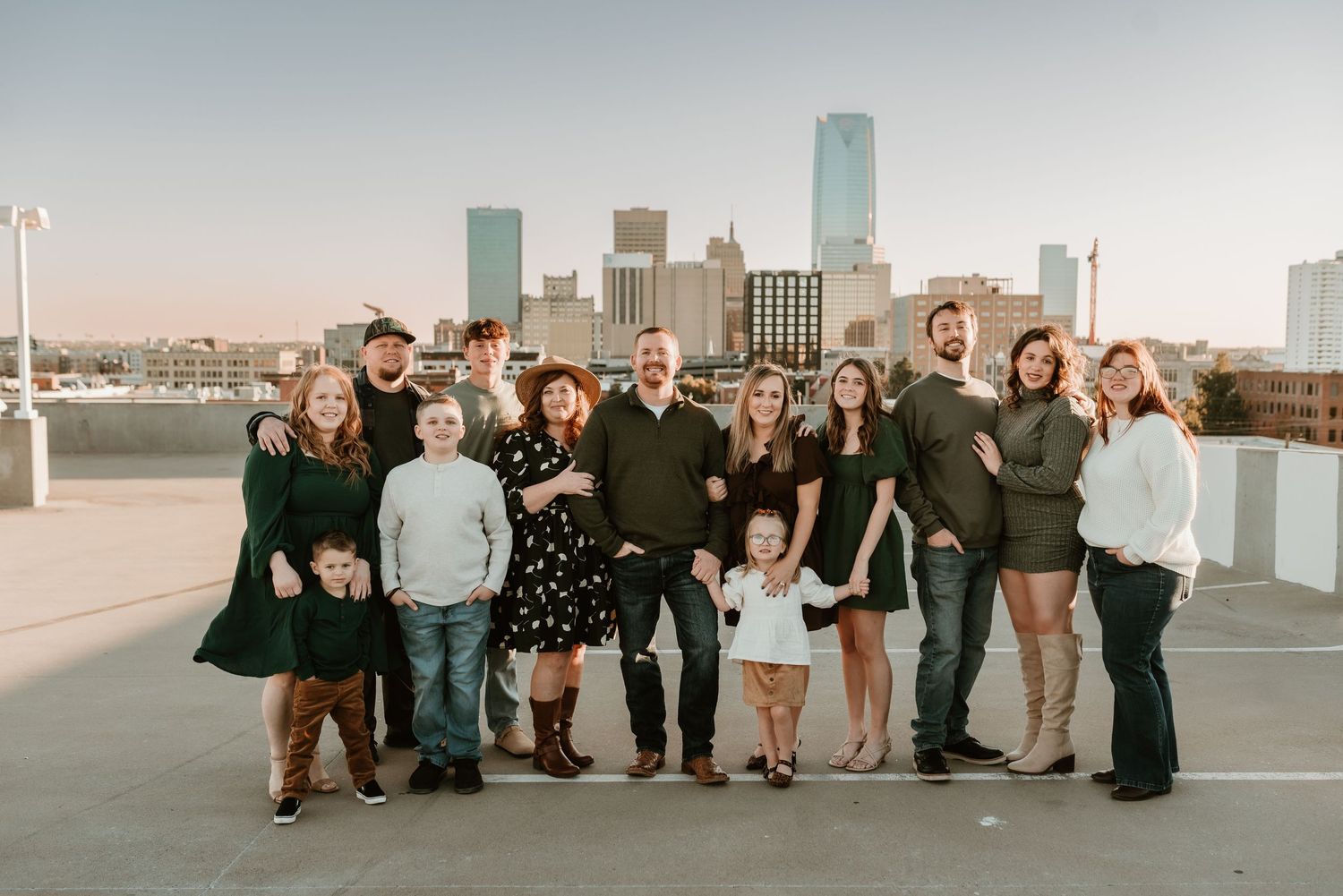 Large extended family group photo on rooftop with downtown city skyline at dusk.