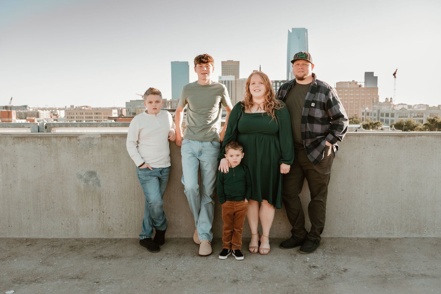 Family of five poses on urban rooftop with city skyline backdrop at sunset.