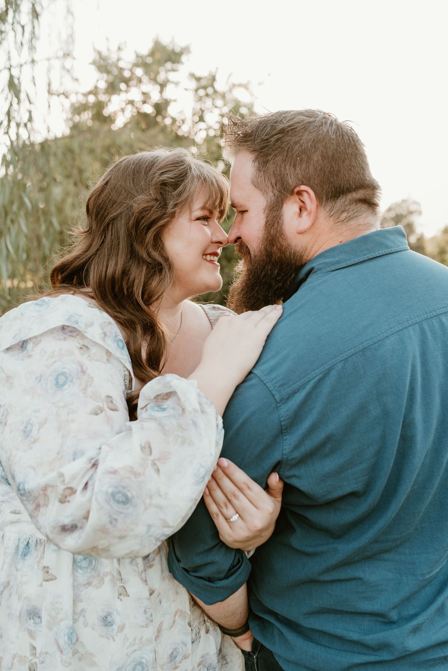 A happy couple smiles and embraces closely, nearly touching noses in golden afternoon light.