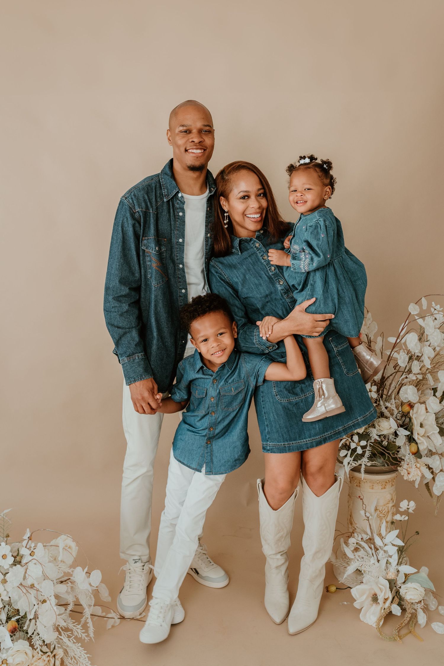 Happy family of four in coordinating denim outfits poses together in a studio setting.